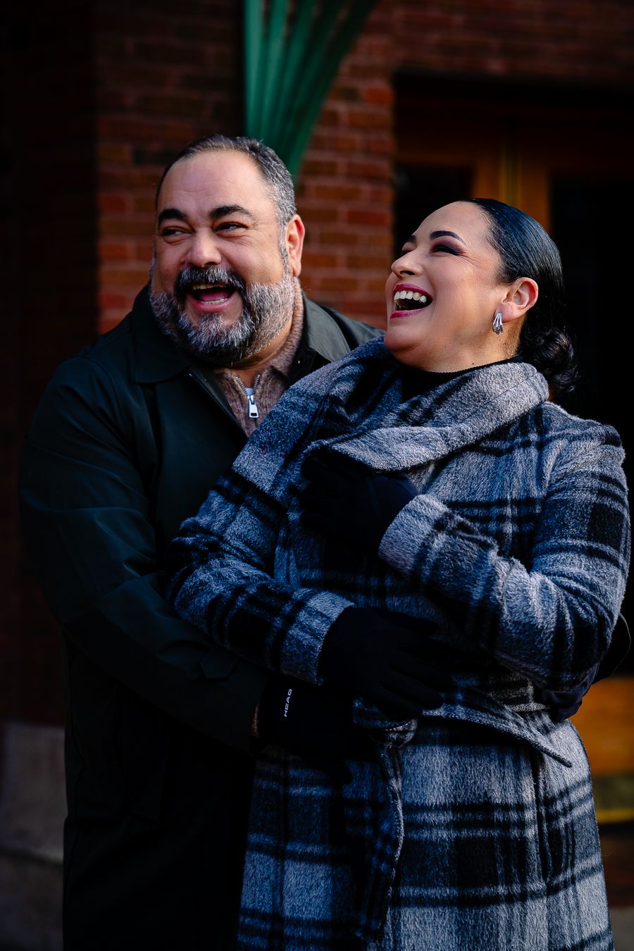 Couple sharing a joyful moment together against brick wall background.