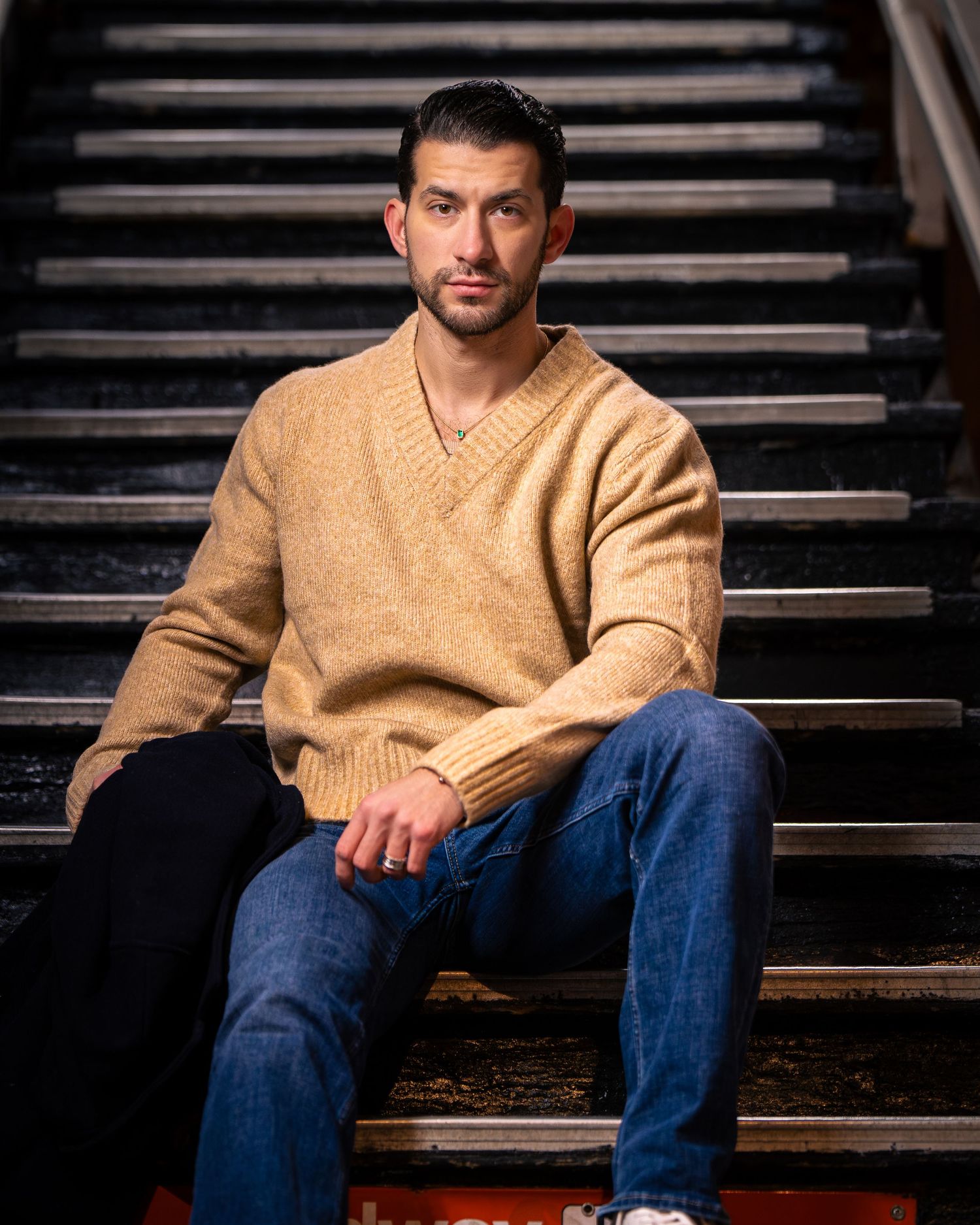 Man in casual tan sweater and jeans seated on dark wooden steps.