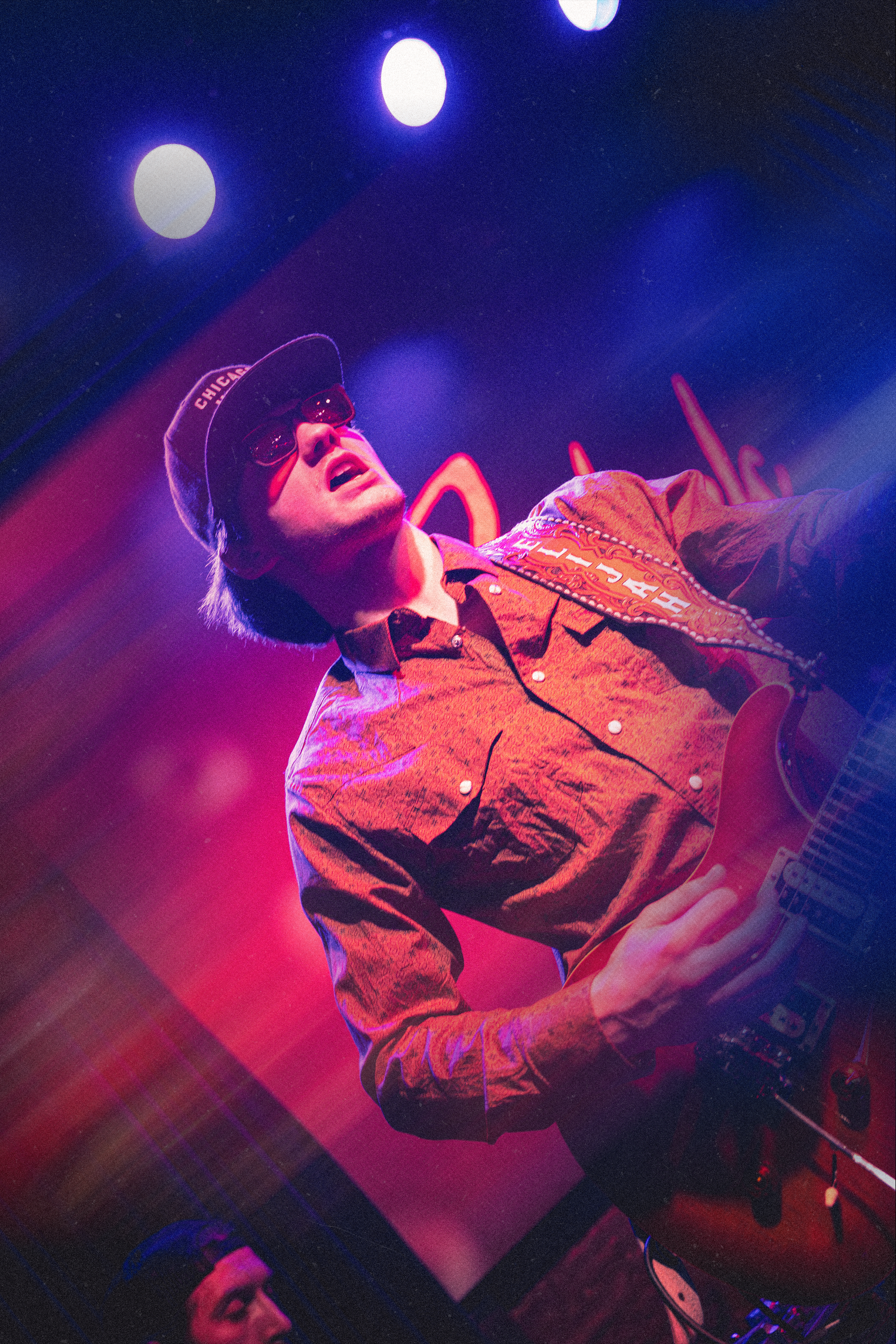 Concert performer dances energetically on stage under dramatic blue and red lighting during a live music performance.