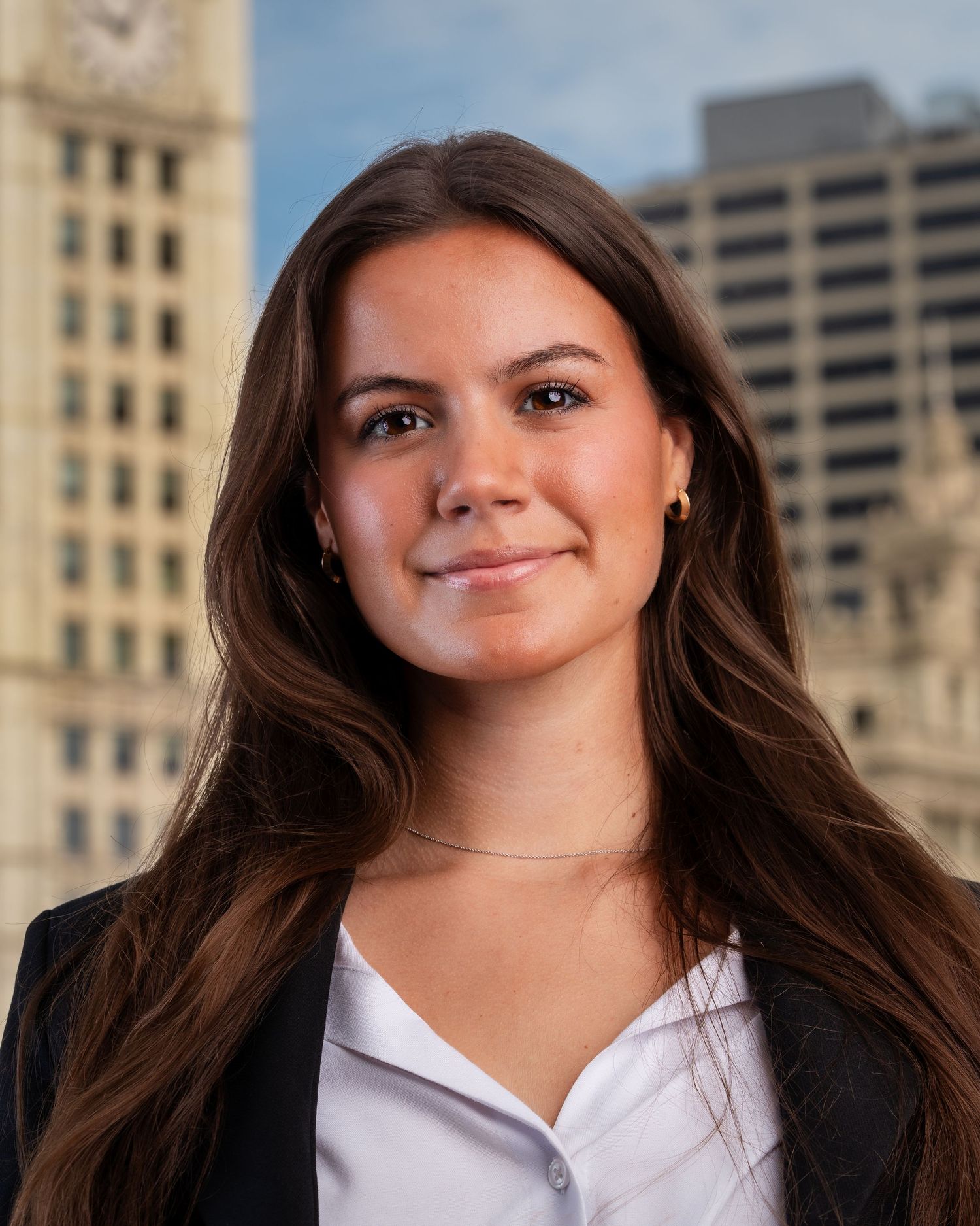 Professional headshots with black blazer and white collar against city buildings.