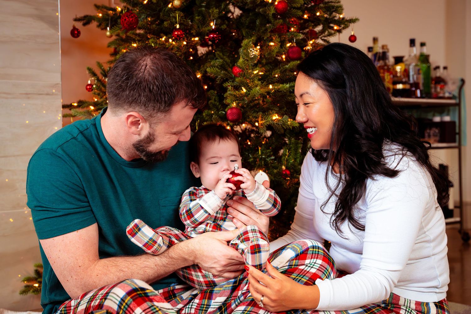 Family enjoying playful moments together by Christmas tree with matching holiday outfits.