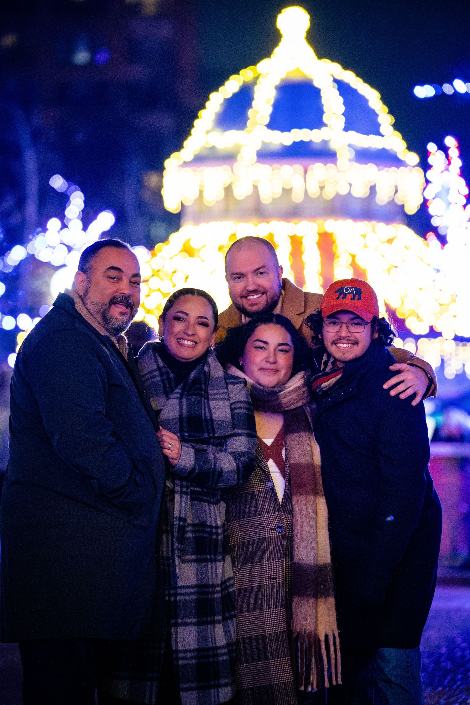 A group stands together at night with illuminated holiday lights and a domed structure glowing in the background.