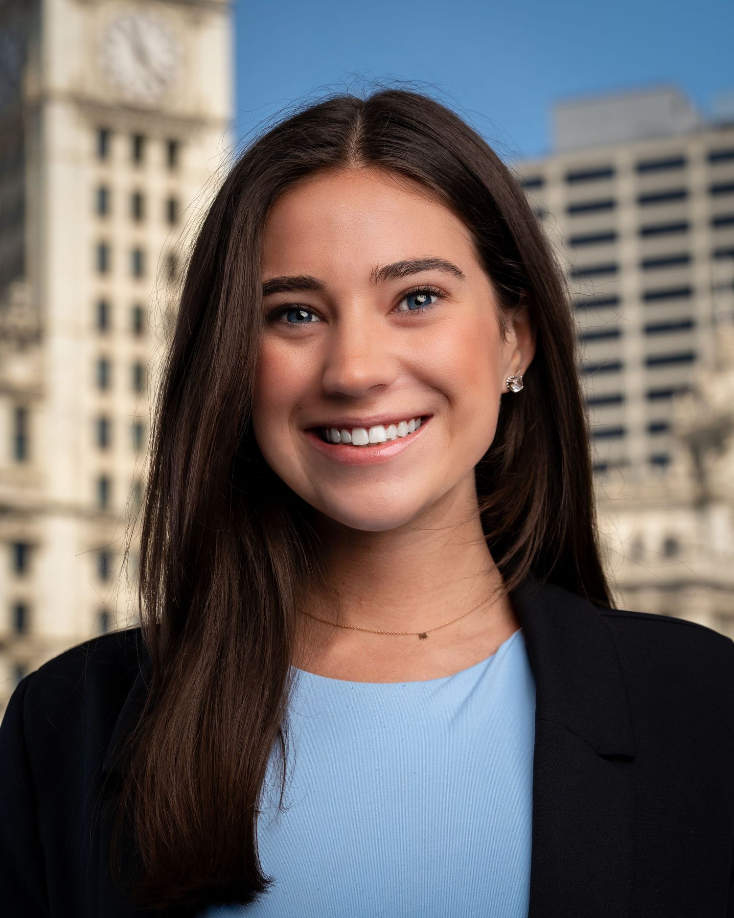 Professional portraits showing person in black blazer and light blue top against city building.