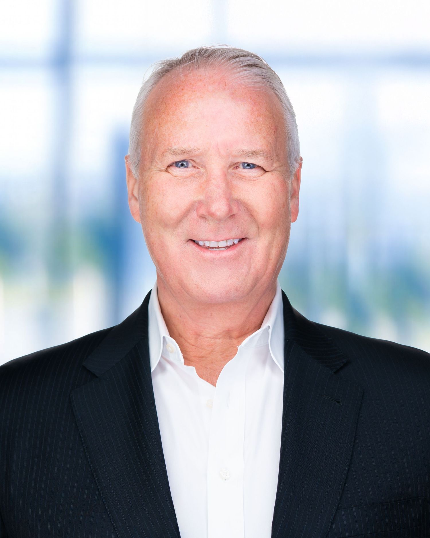 Corporate portrait of person in white dress shirt and dark suit against modern office setting.
