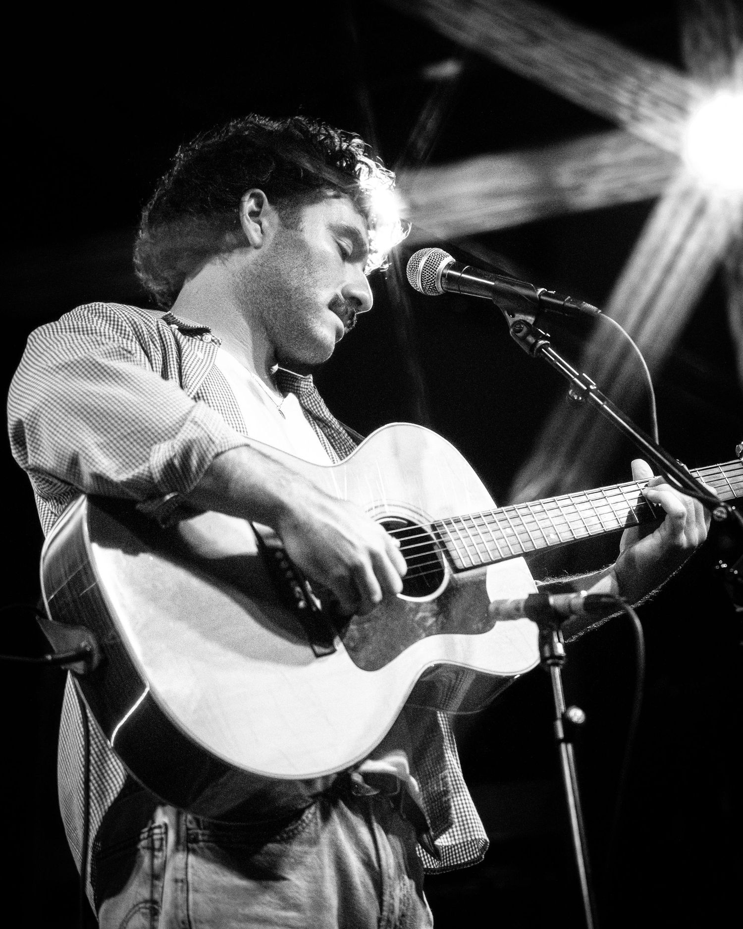 Black and white concert photo showing musician strumming acoustic guitar on stage.