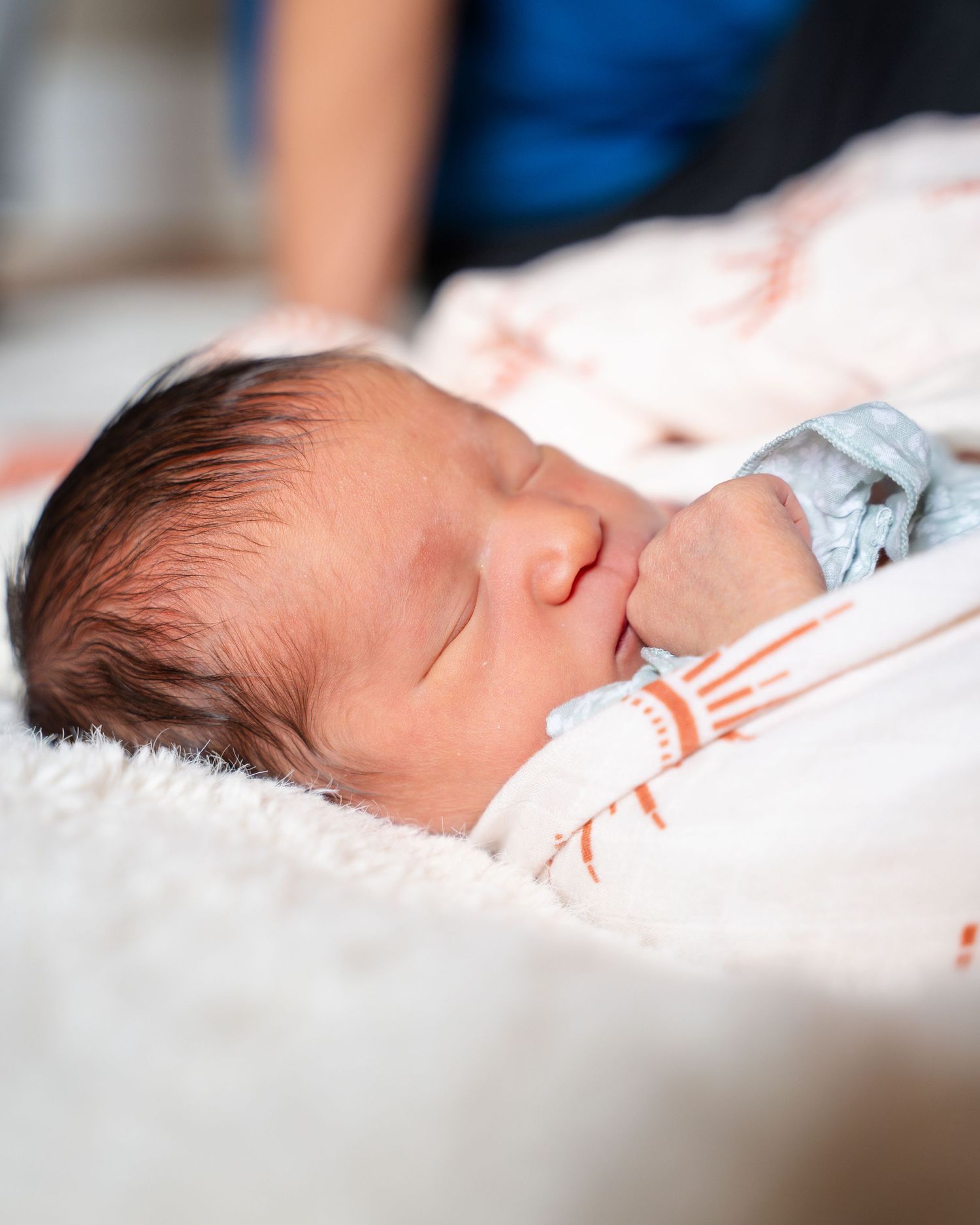 A peaceful newborn baby sleeping soundly on white bedding wearing a striped outfit.