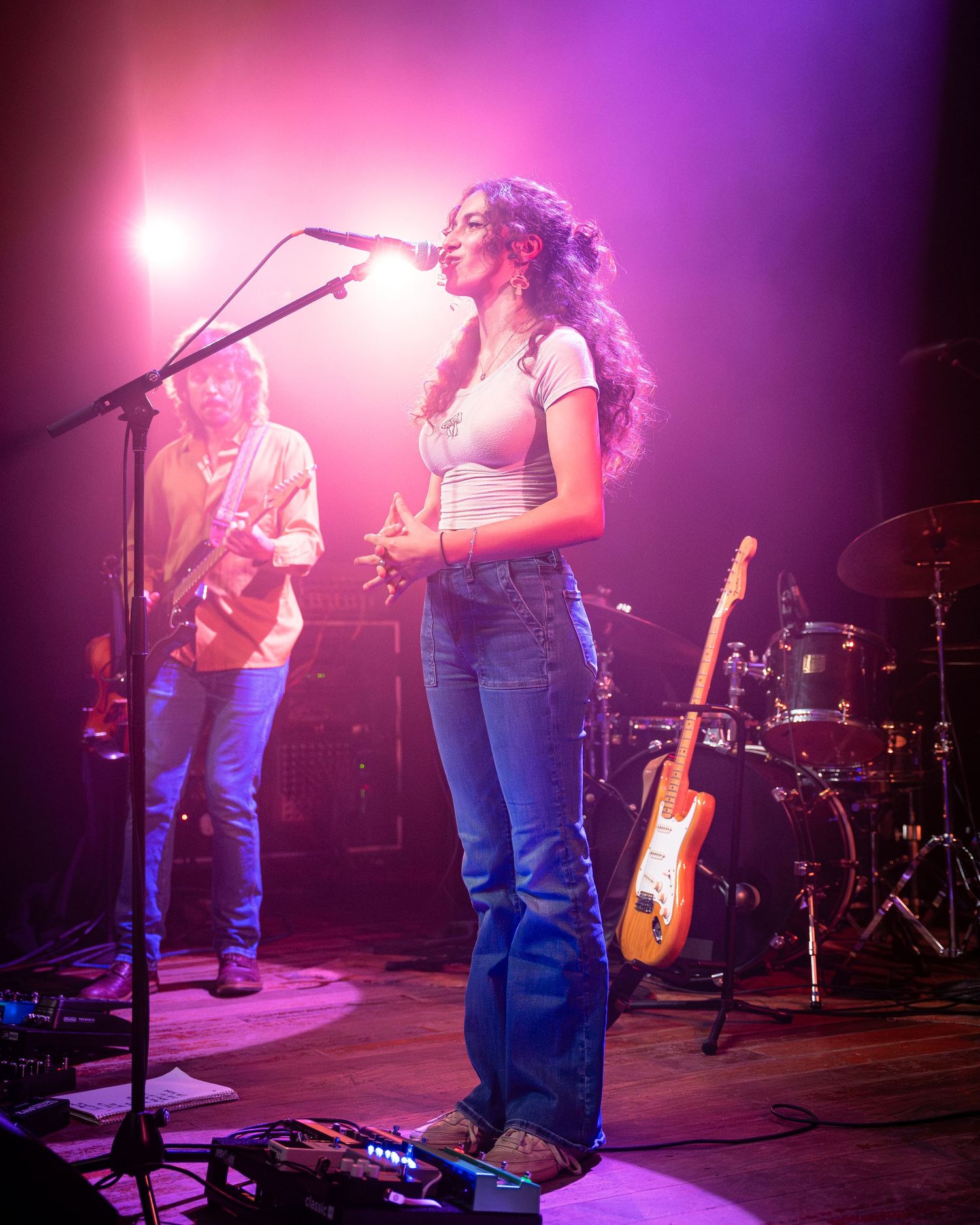 Concert stage bathed in pink and purple lighting showing performers in casual attire.