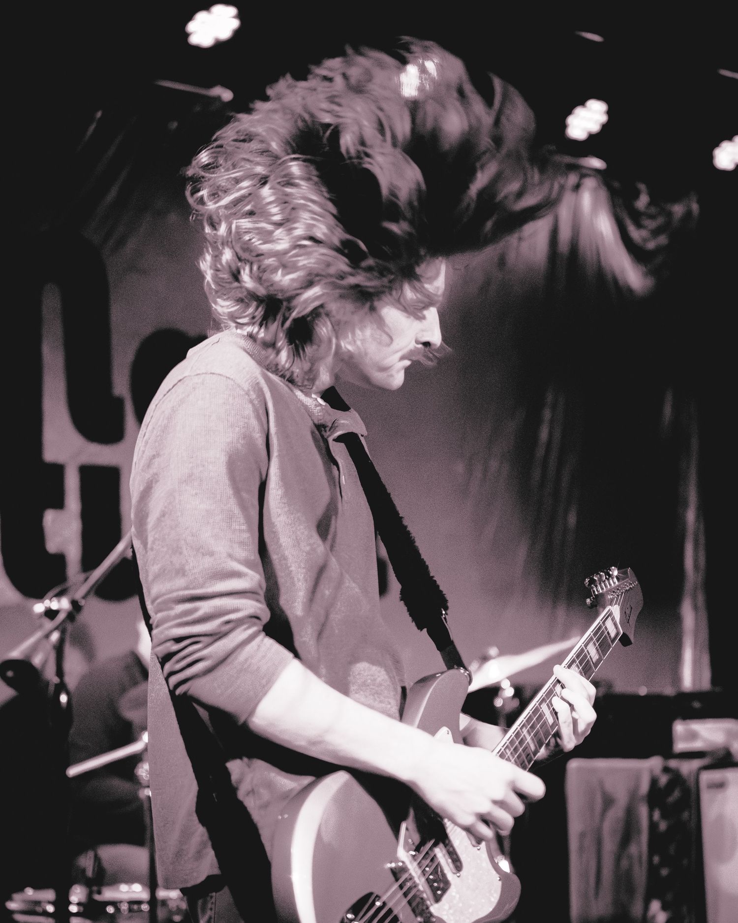 A musician performs energetically with a guitar on stage in a black and white photograph.