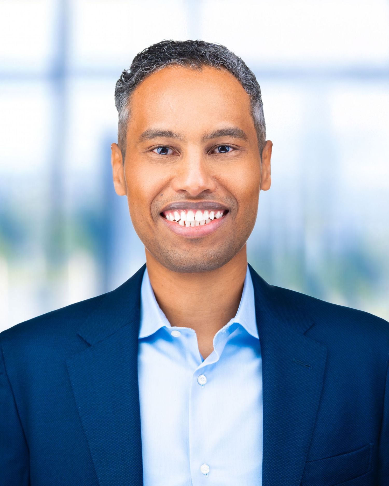 Business headshot of person wearing blue suit jacket and dress shirt with bright window lighting.
