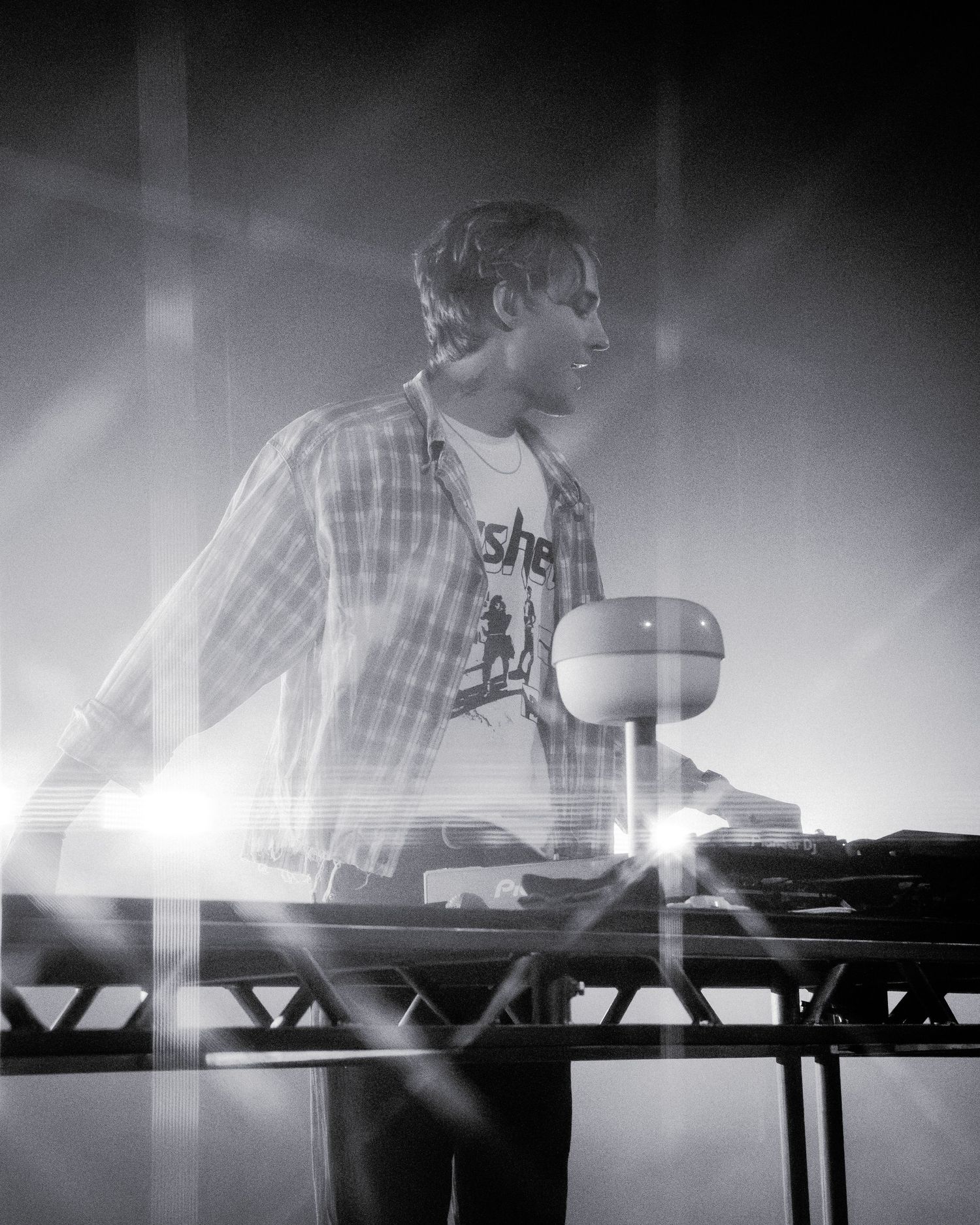 Black and white photo of musician performing at electronic music setup with dramatic lighting.