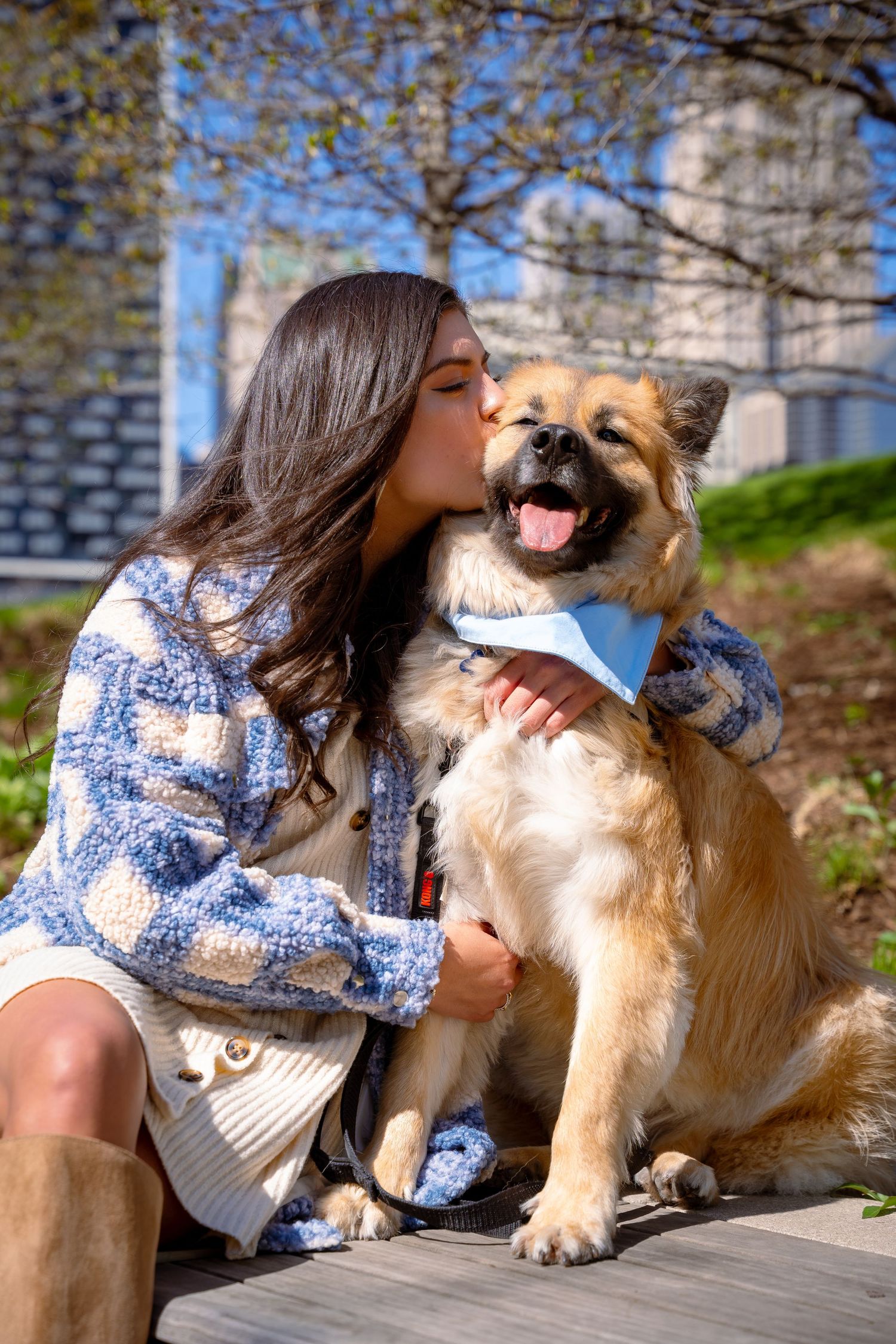Person in blue patterned top sharing affectionate moment with golden retriever dog outdoors.