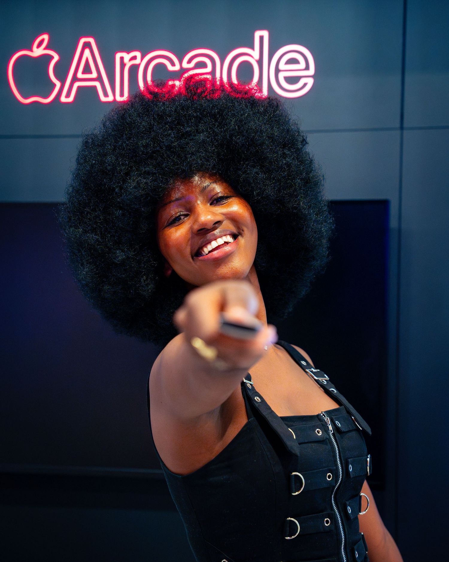 Performer smiles beneath neon Arcade sign in stylish black outfit.
