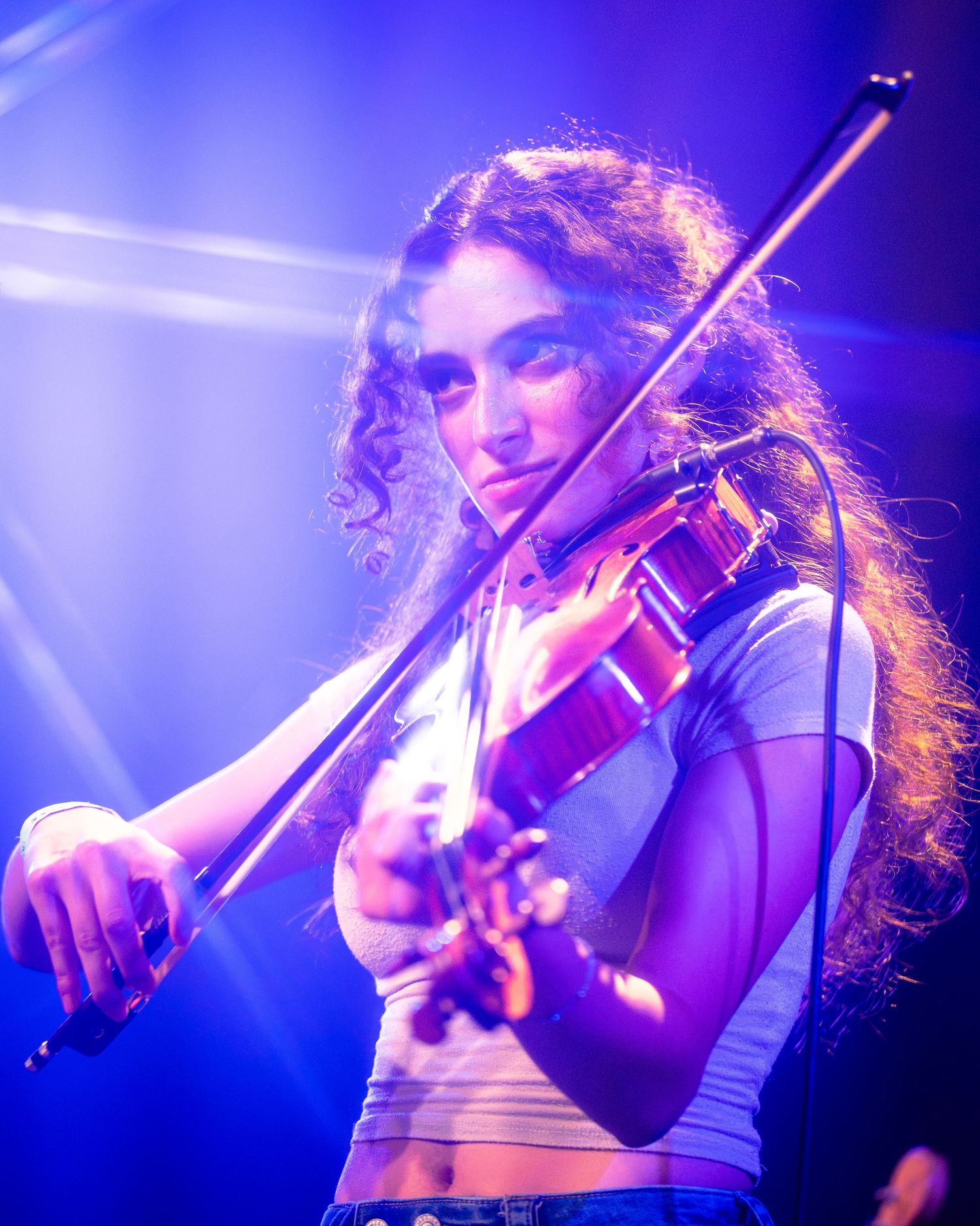 Violinist plays passionately under blue stage lights during performance.