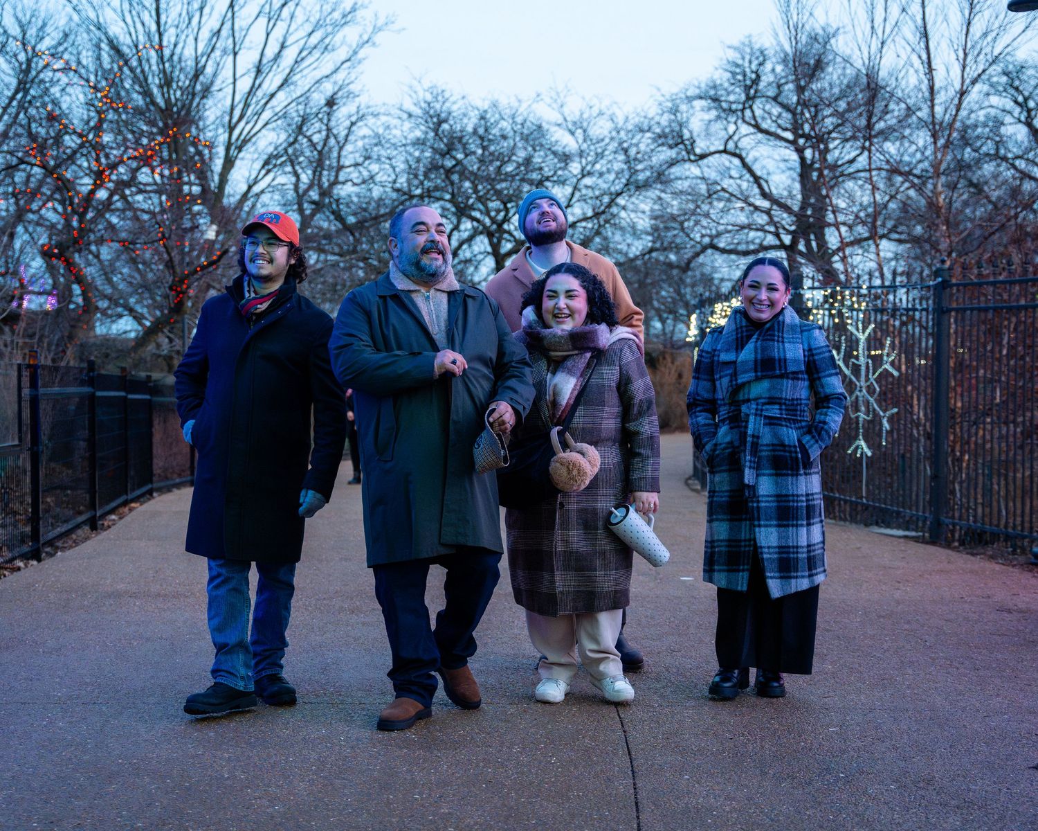 A group of people bundled up in winter coats stand together on a walkway during a cold winter day.