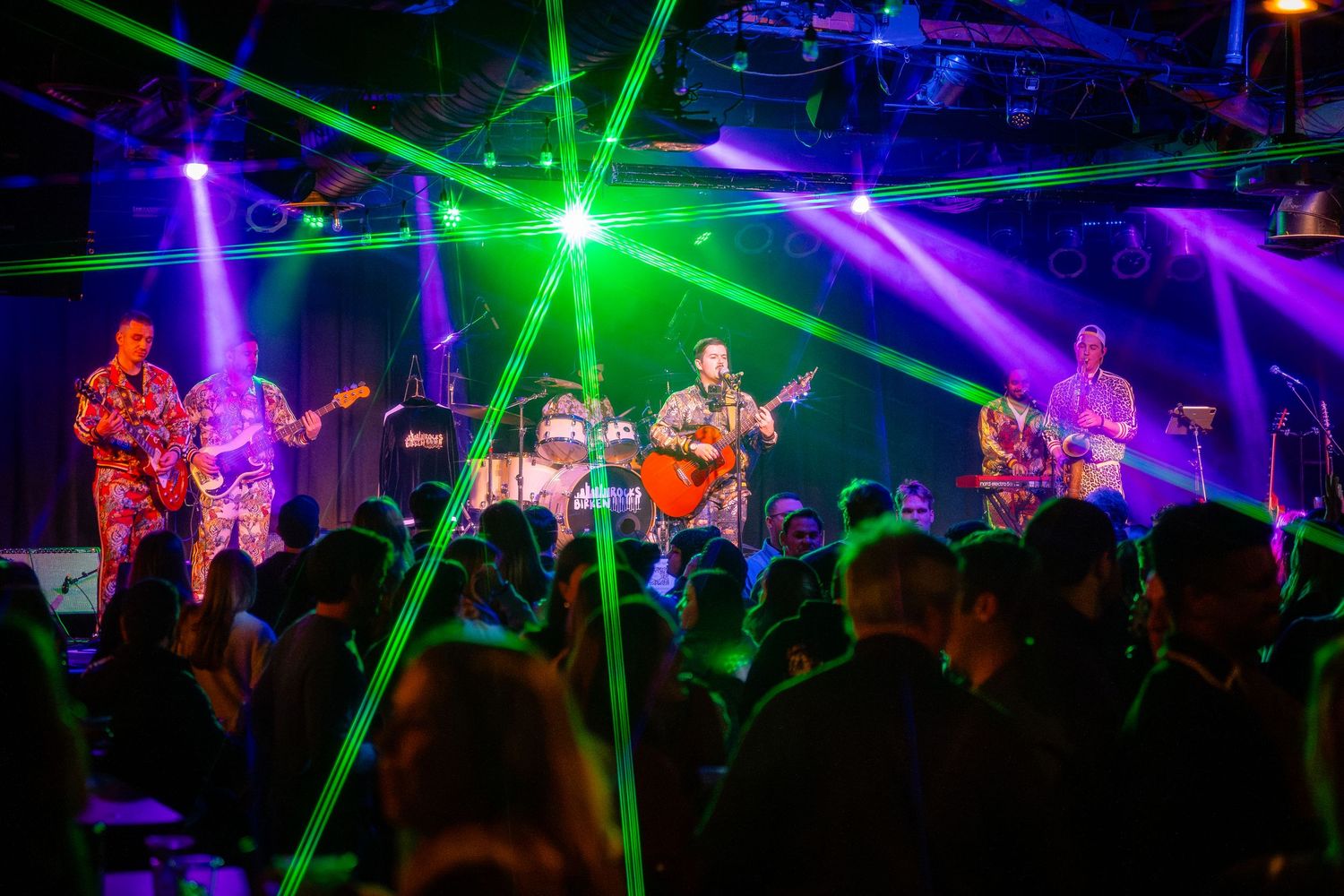 Concert venue illuminated with colorful laser lights and crowd silhouettes.