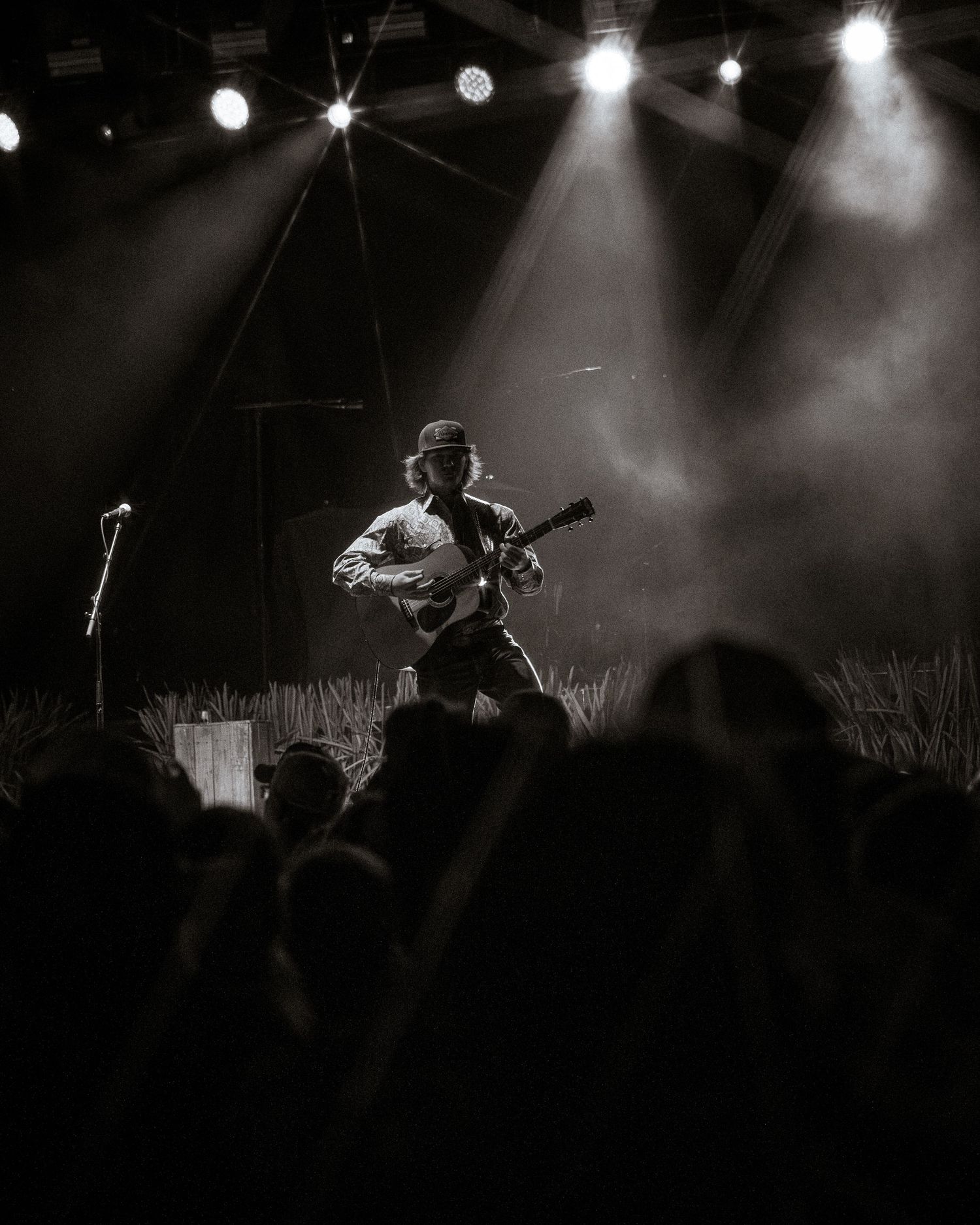 Concert crowd silhouette with dramatic stage lighting and performer on stage.