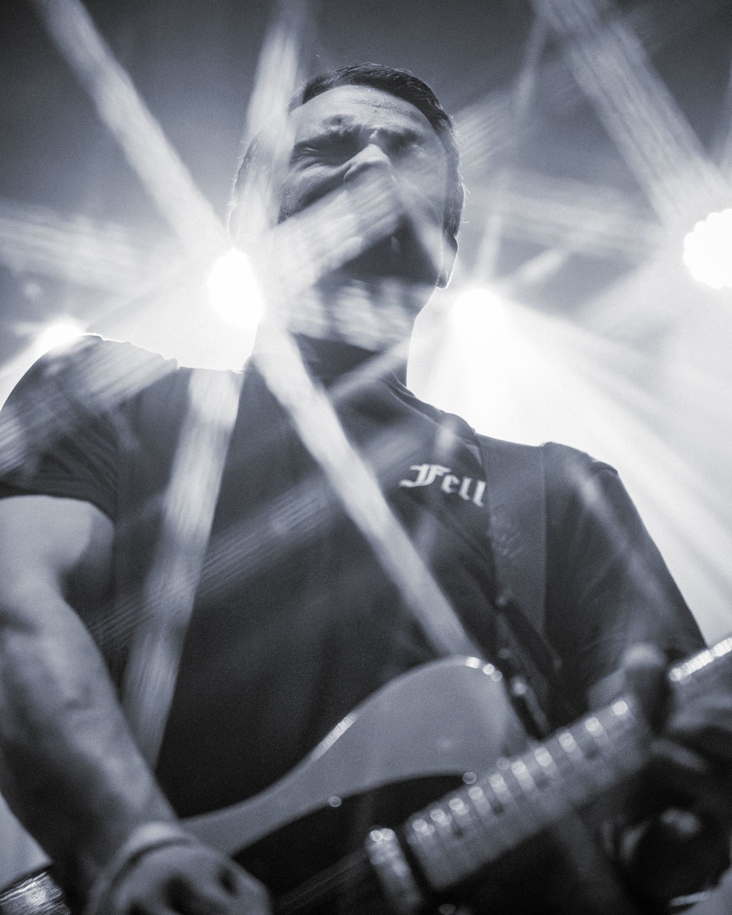 Dramatic black and white concert photo with bright stage lights creating rays through smoke.