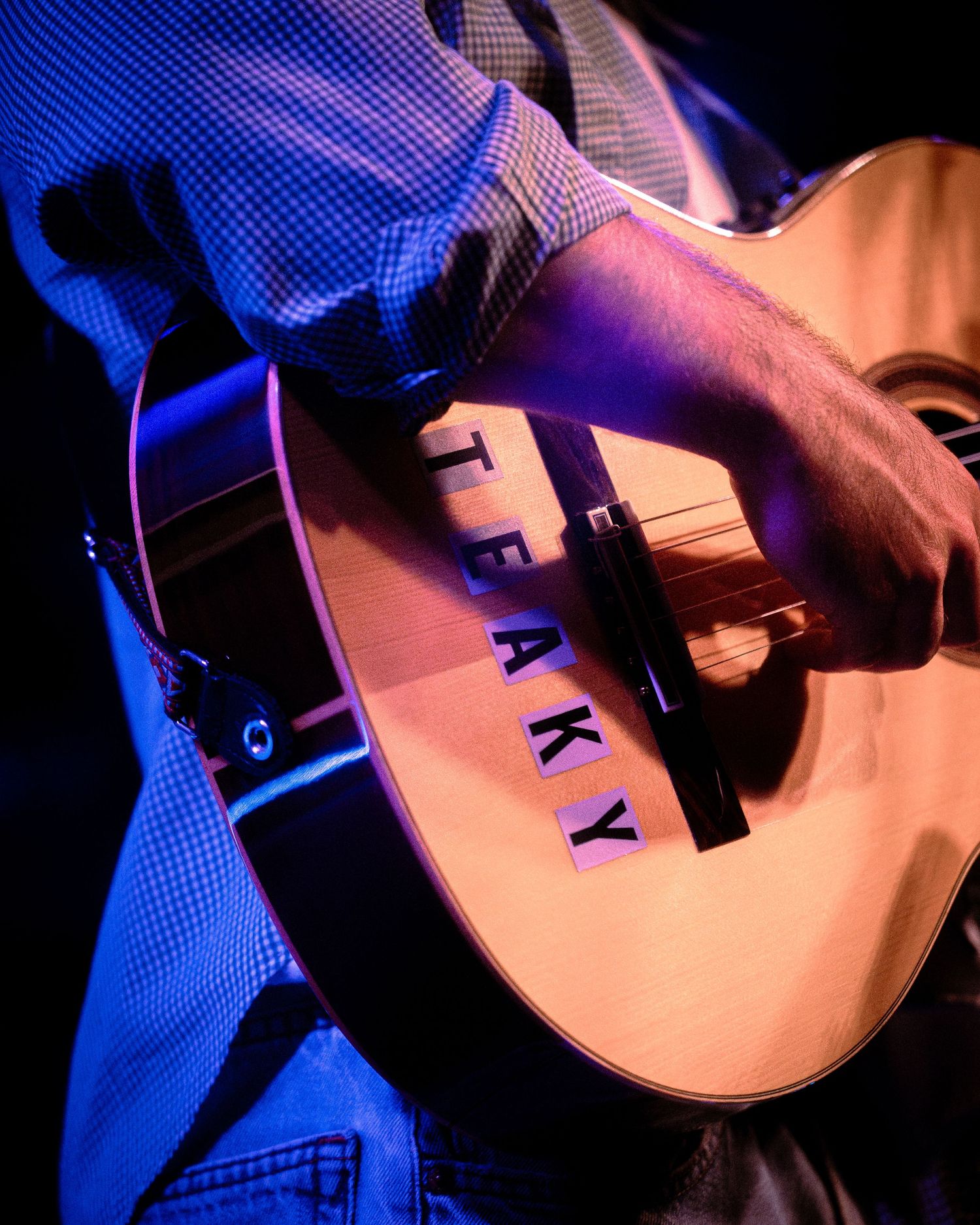 Close-up detail of acoustic guitar being played under blue stage lighting.
