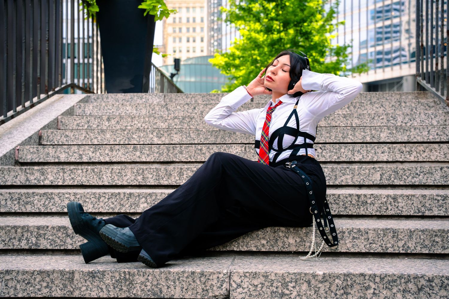 Model poses on granite steps with urban architecture and greenery in background.