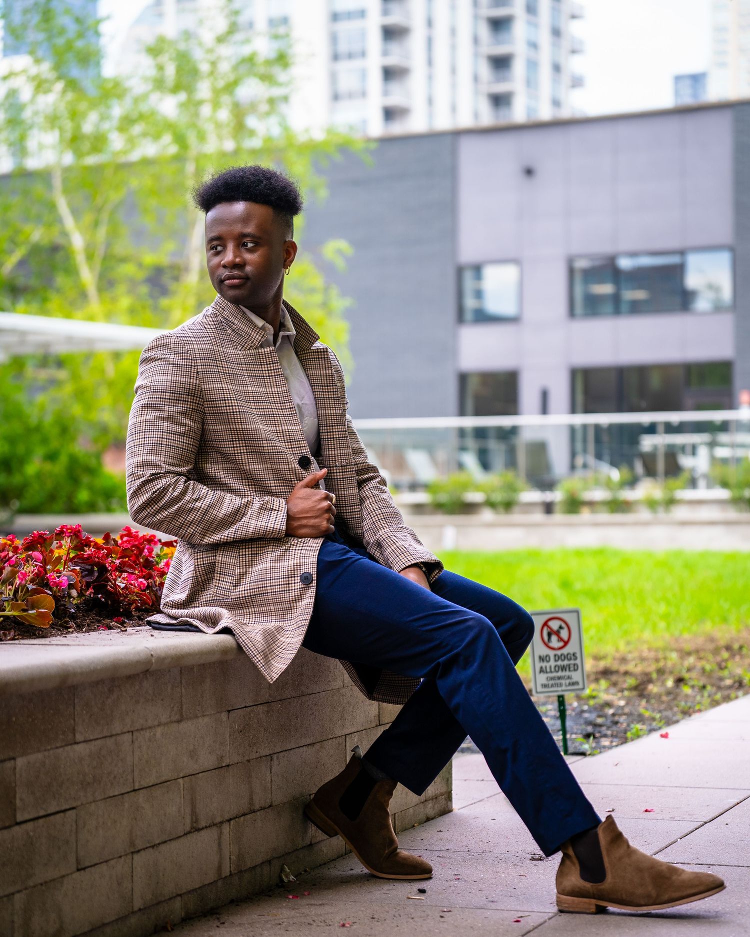 Person in plaid blazer sitting on concrete ledge in urban setting.