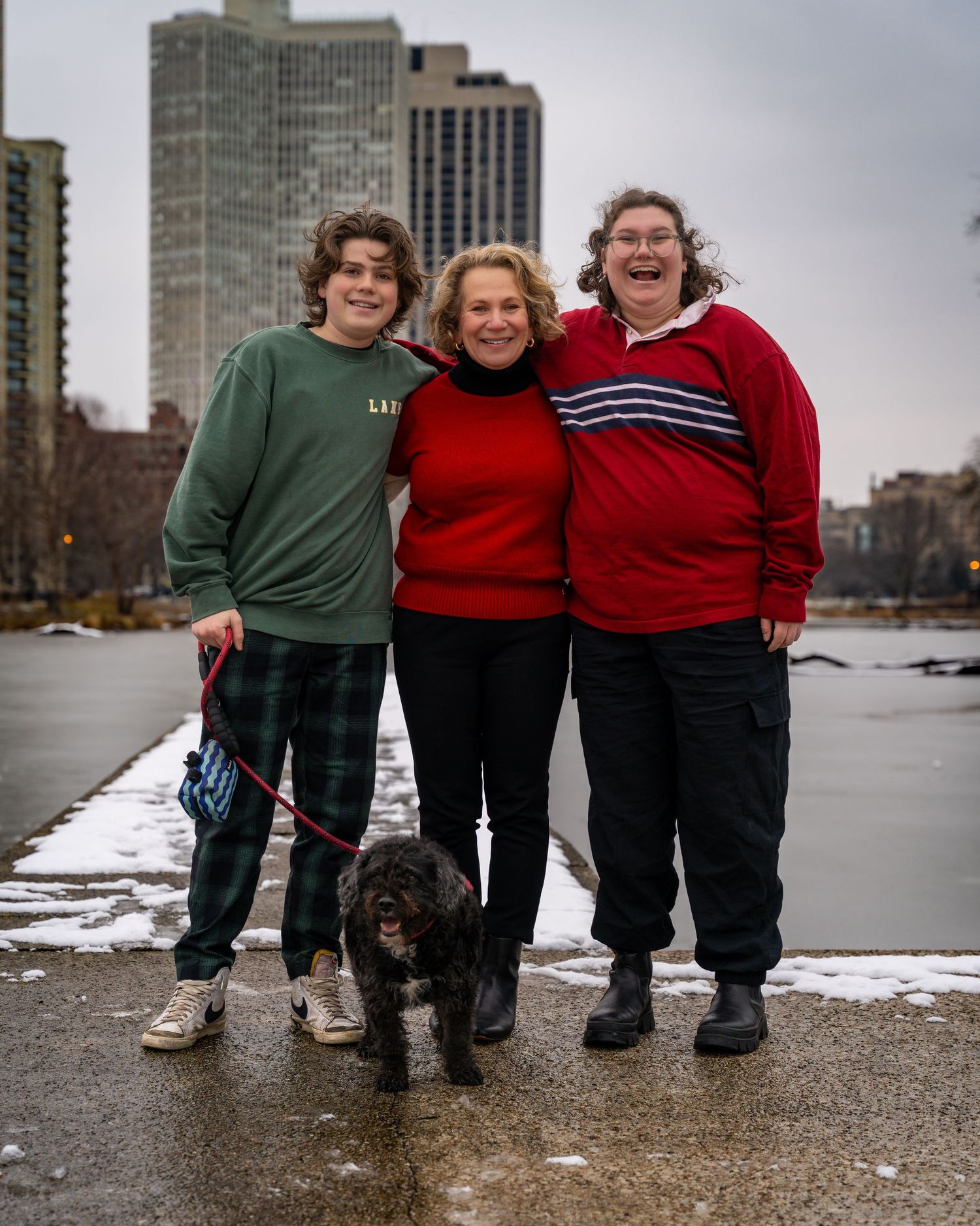Three people stand together on a snowy urban path with tall buildings visible in the background.