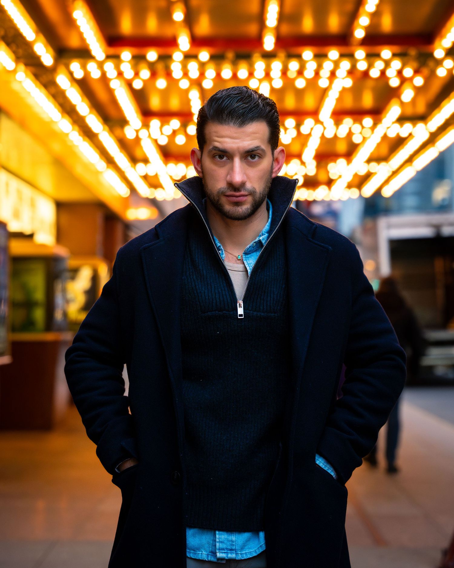Night portrait with warm carnival lights and dark jacket creating moody atmosphere.