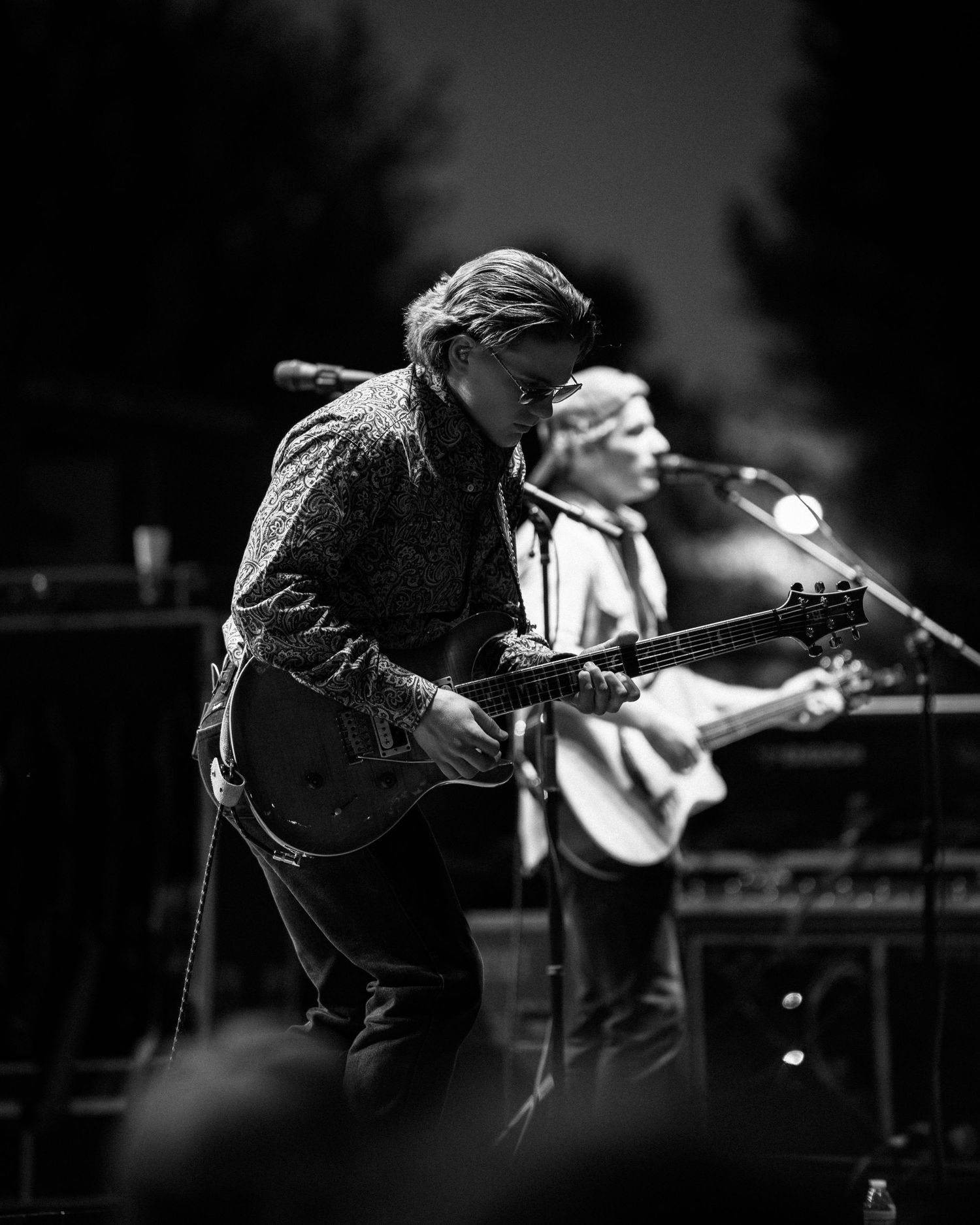 Black and white concert photo showing musicians performing with guitars on dimly lit stage.