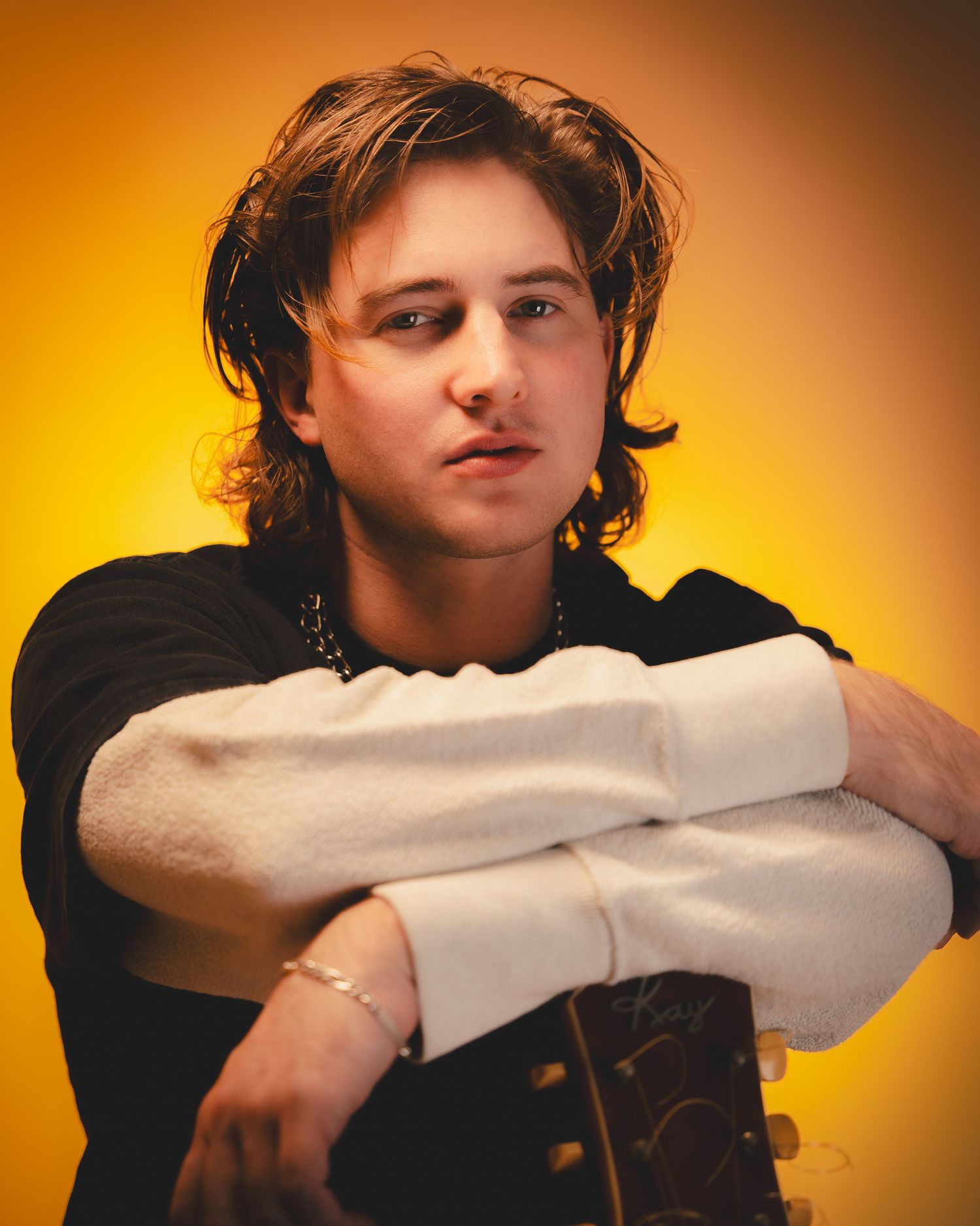 Close-up portrait with dramatic lighting showing a musician resting on crossed arms.