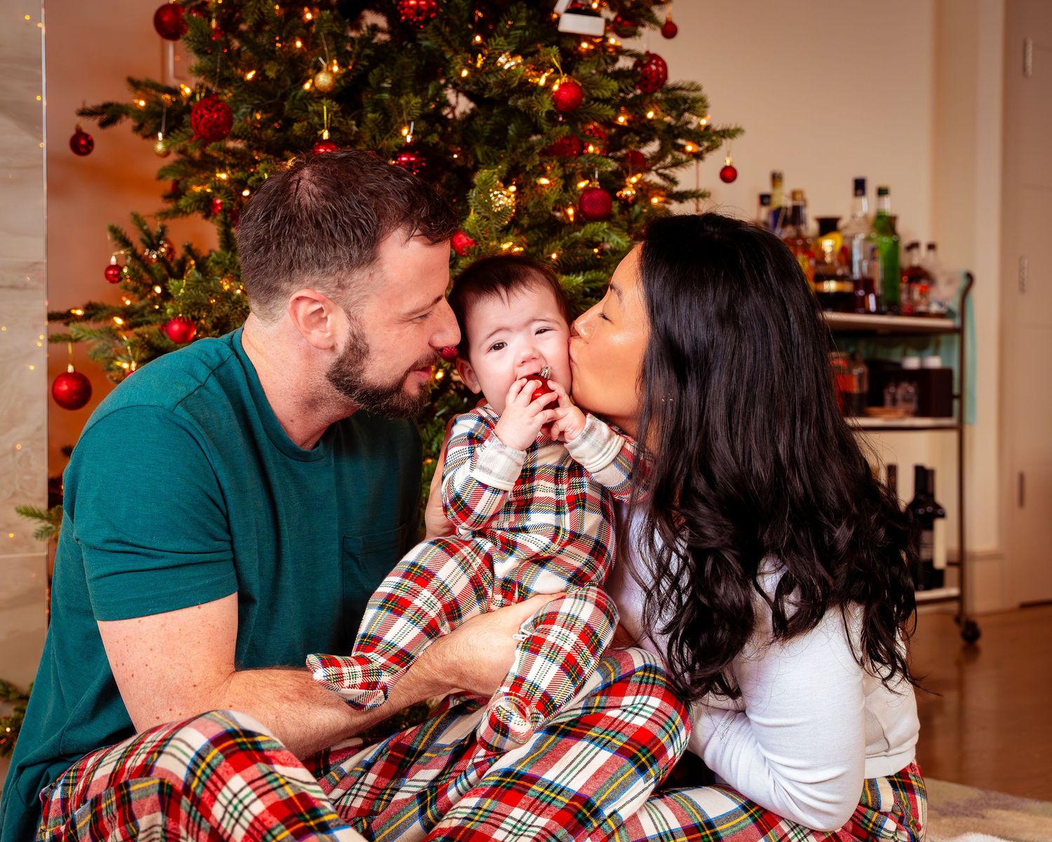 A group in matching plaid pajamas sits together in front of a decorated Christmas tree with twinkling lights.