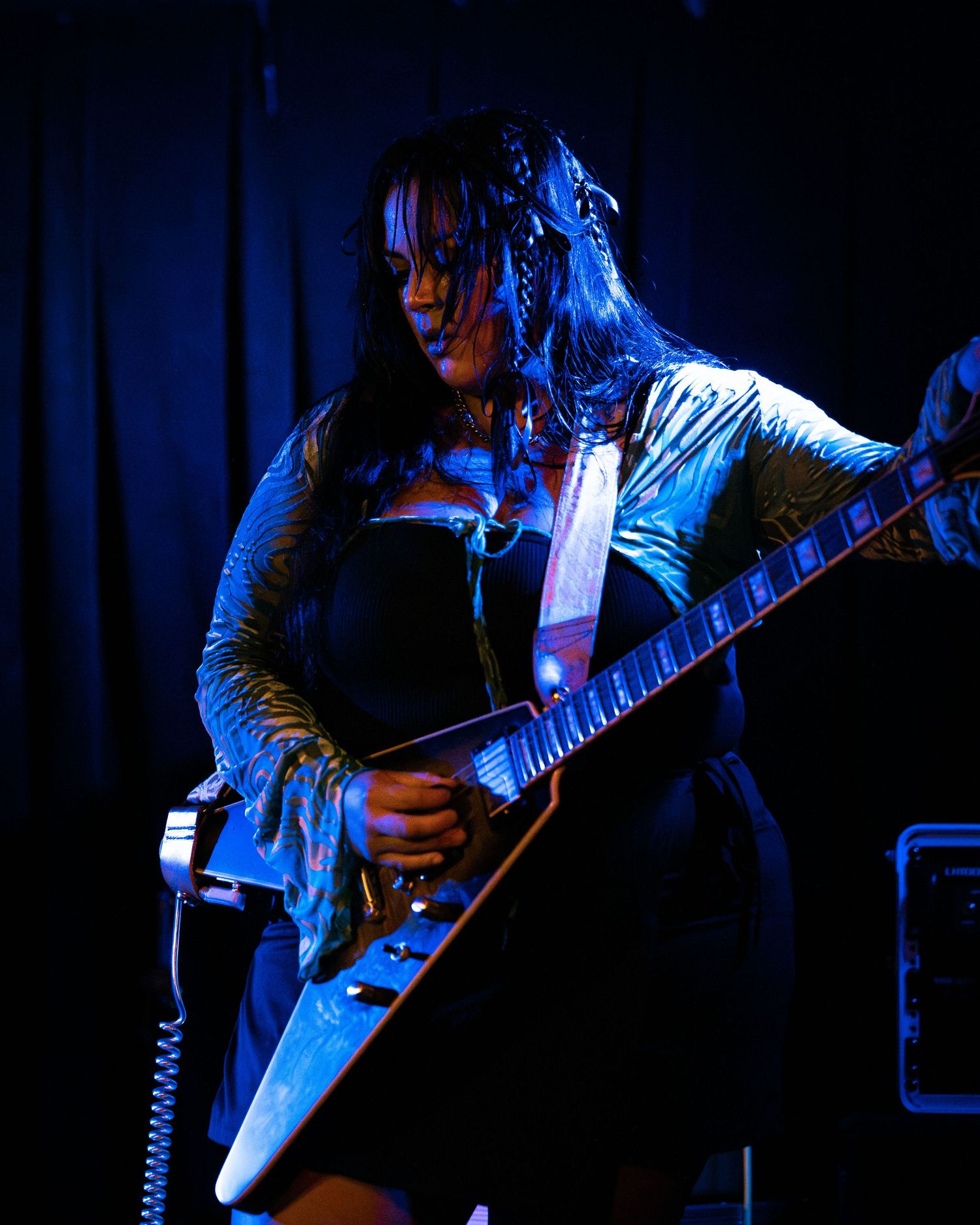 Electric guitarist performs under moody blue stage lighting during concert.