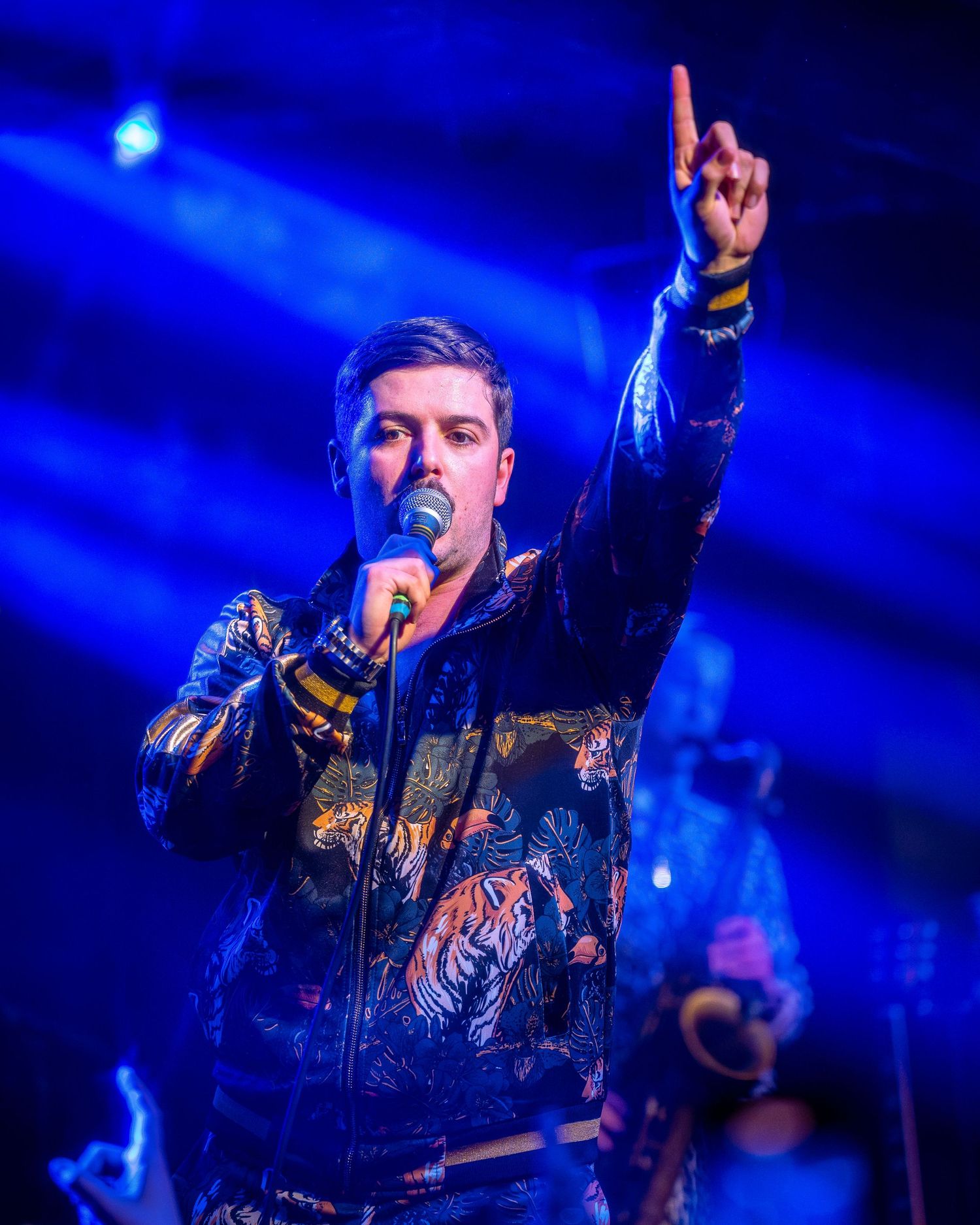 Energetic stage performance with dramatic blue lighting and raised hand gestures.