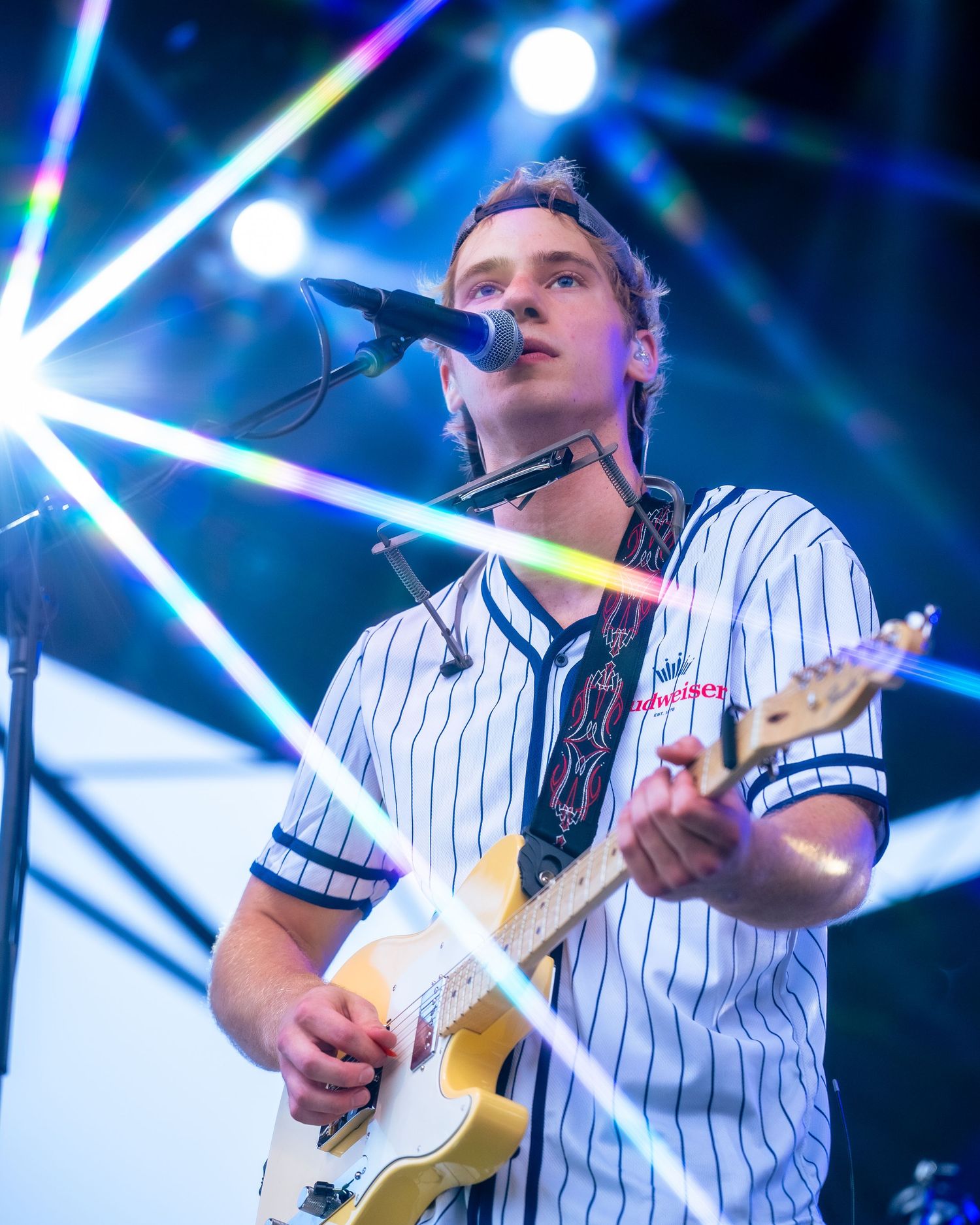 Musician in baseball jersey playing guitar against backdrop of colorful stage lighting effects.