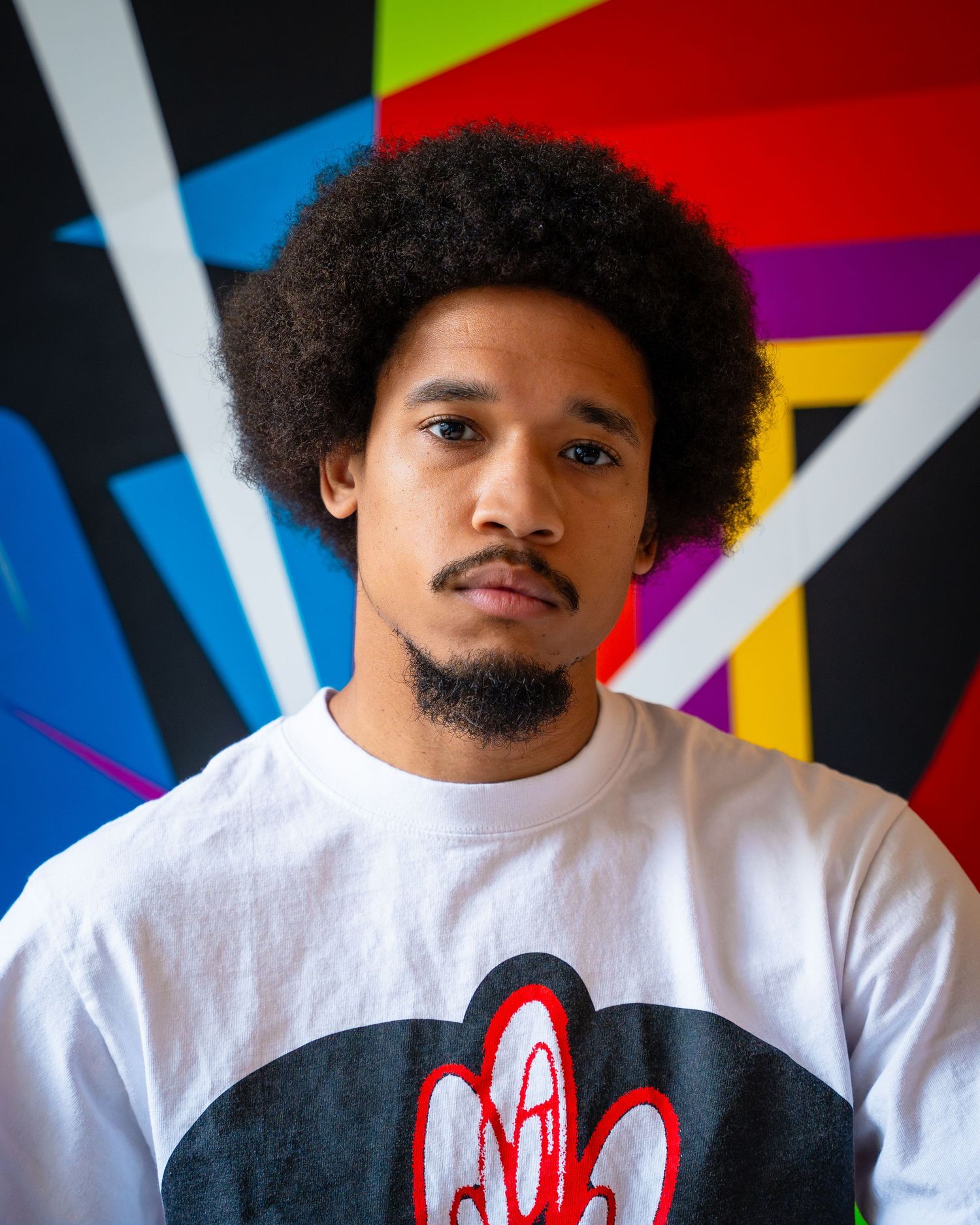 Portrait against vibrant geometric mural backdrop featuring white graphic t-shirt.