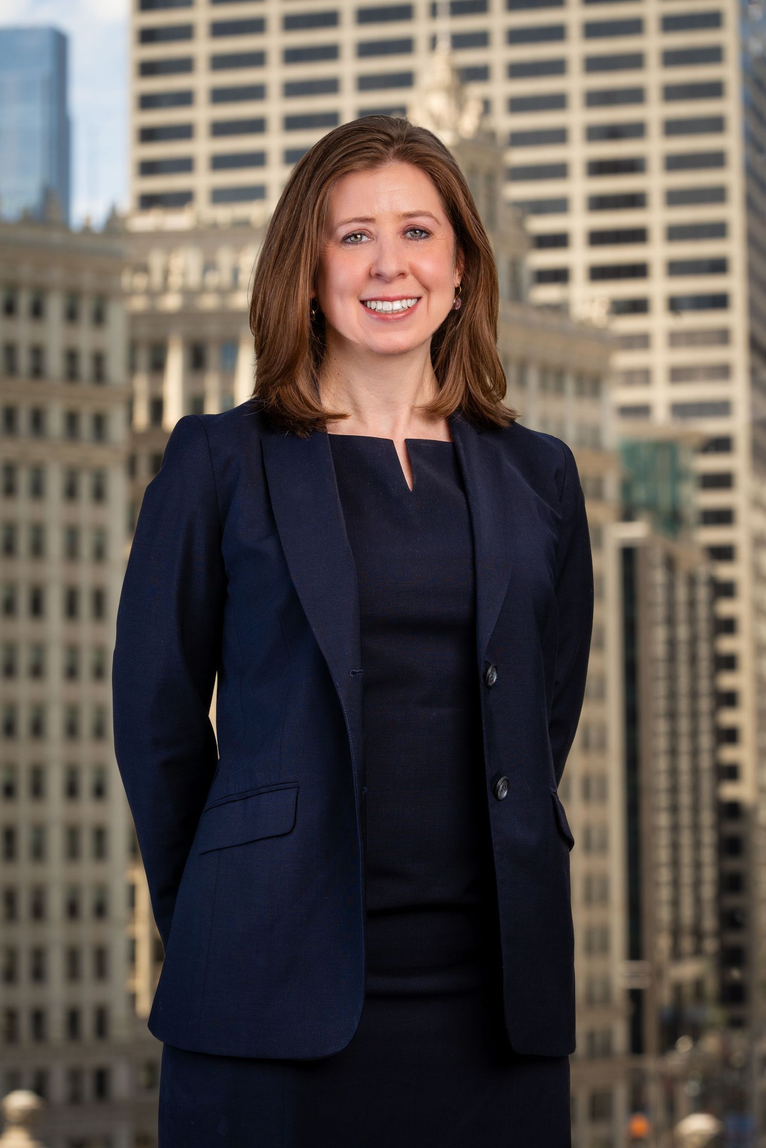 Business portraits in black suit jacket against modern office buildings.