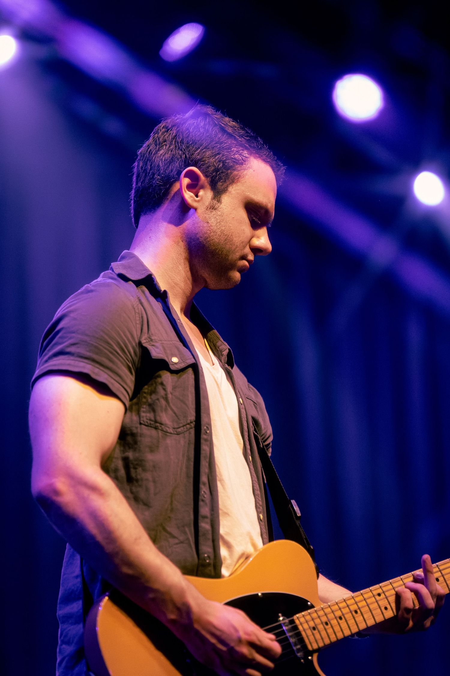 Musician performs on stage with acoustic guitar under purple stage lighting during live concert performance.