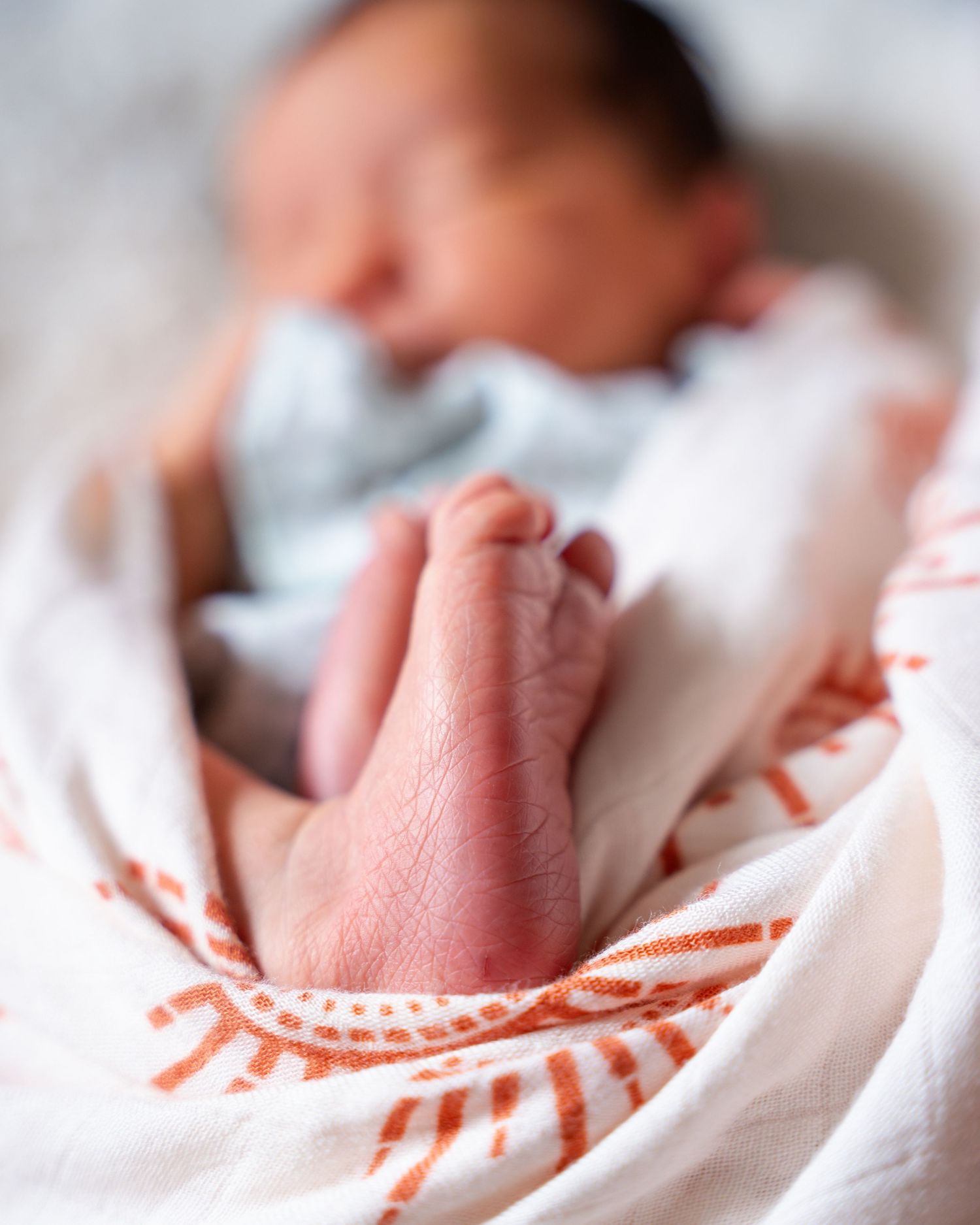 Close-up of baby wearing white and orange patterned clothing while sleeping.
