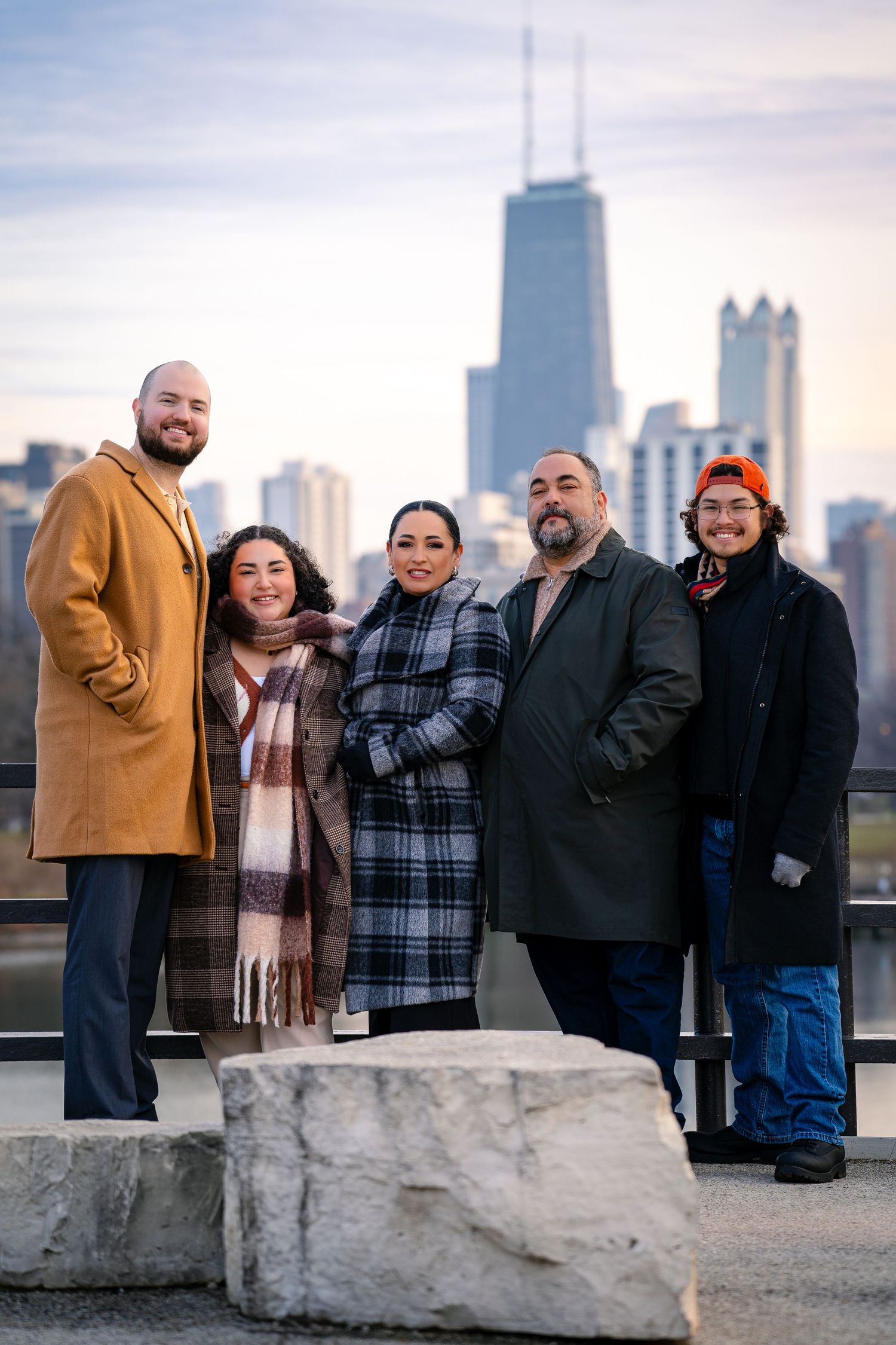 A group of people stand together on a rooftop with the Chicago skyline and John Hancock building visible in the background.