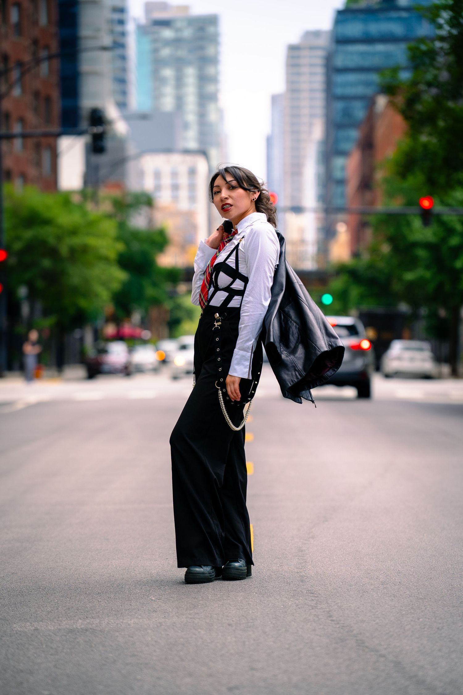 Fashion model poses in black and white outfit on city street with skyscrapers in background.