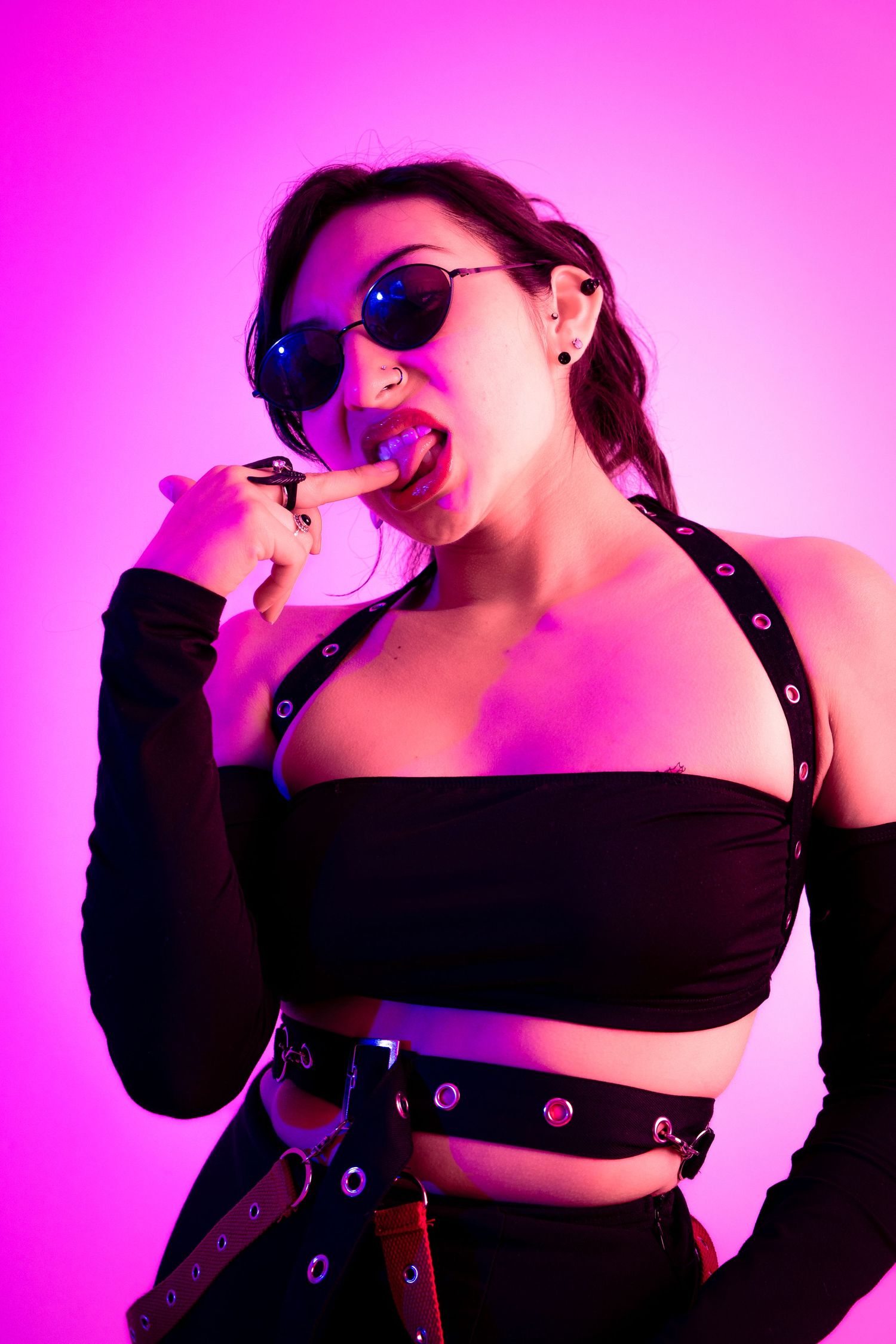 Alternative style portrait with sunglasses and black outfit in pink neon lighting.