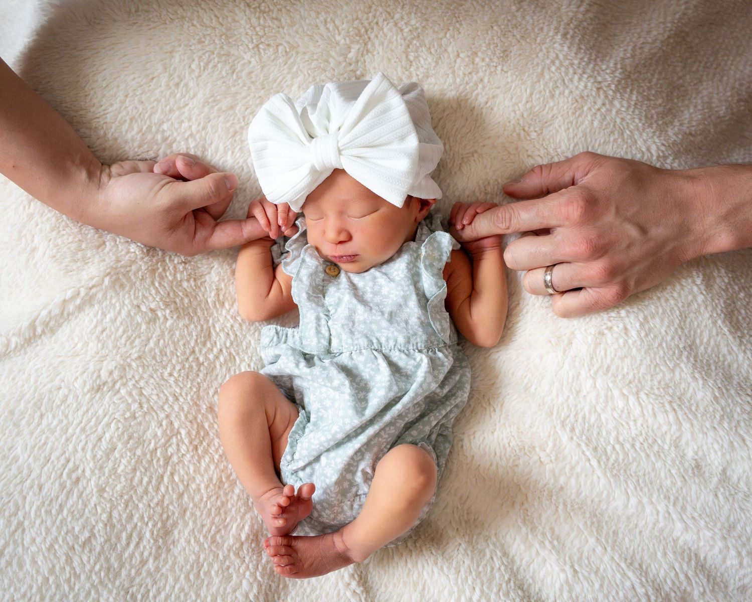 Newborn baby in white lace dress lying on cream textured surface.
