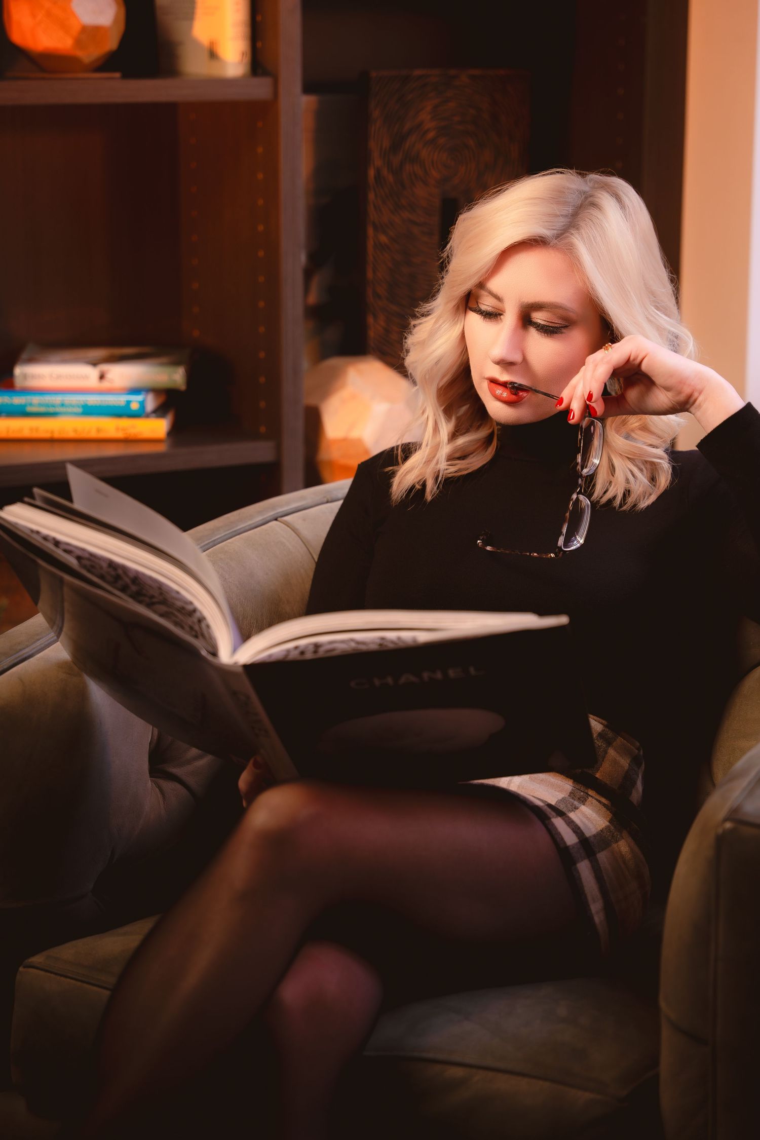 A person with blonde hair reads a book while relaxing on a dark leather couch in warm ambient lighting.