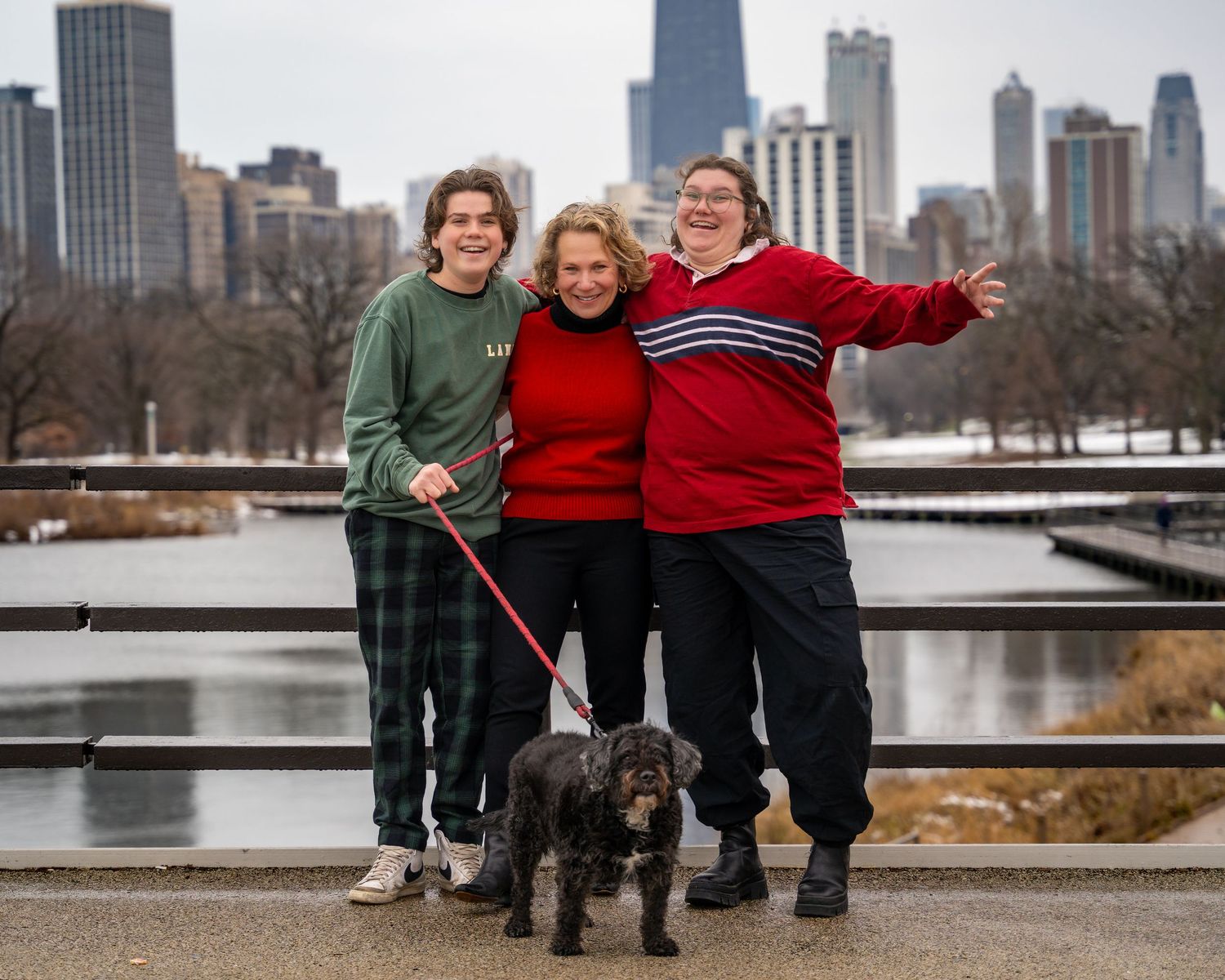 Three people and a black dog pose together on a path with Chicago's downtown skyline in the background.