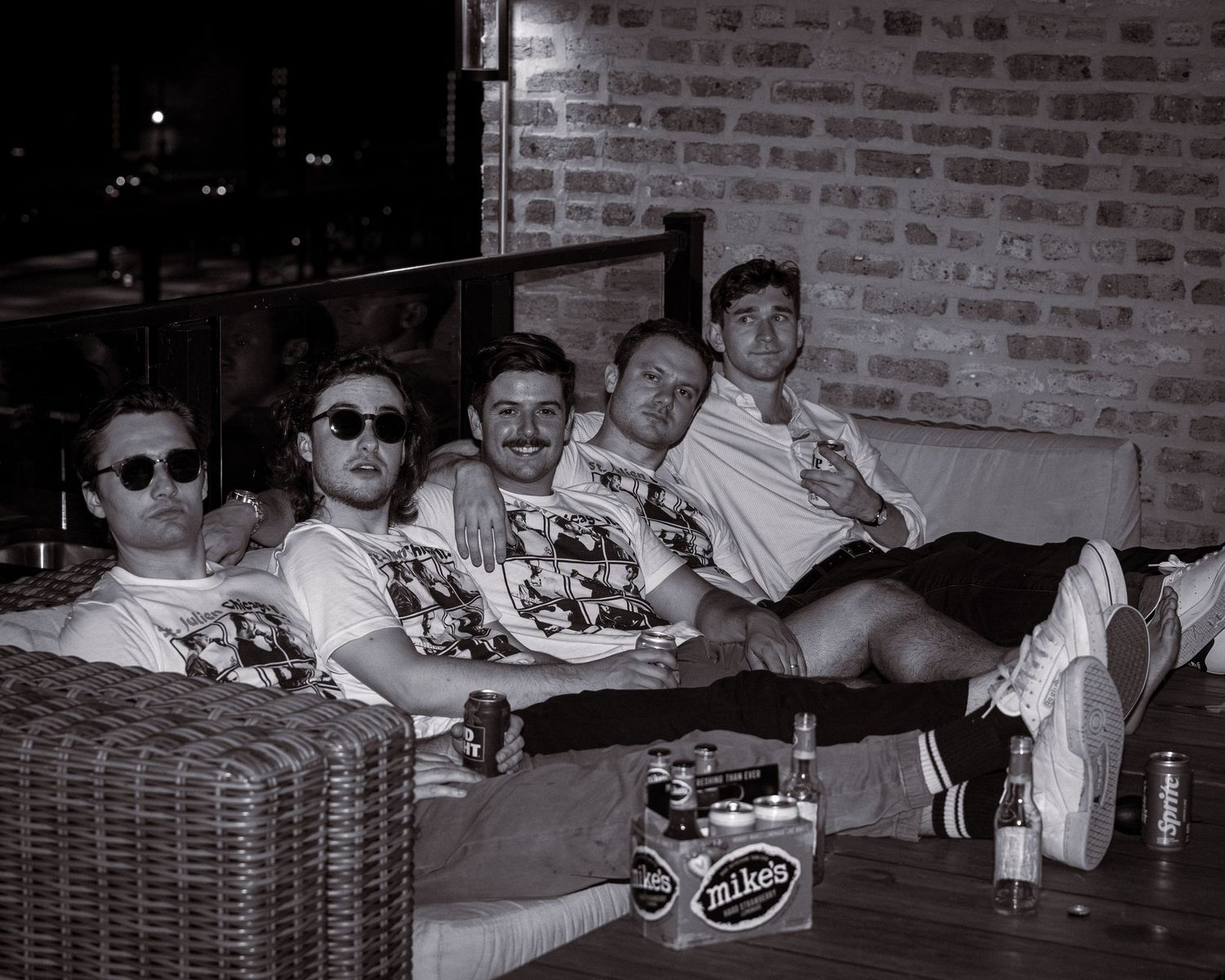 Group lounging on outdoor furniture in casual attire, black and white photo.