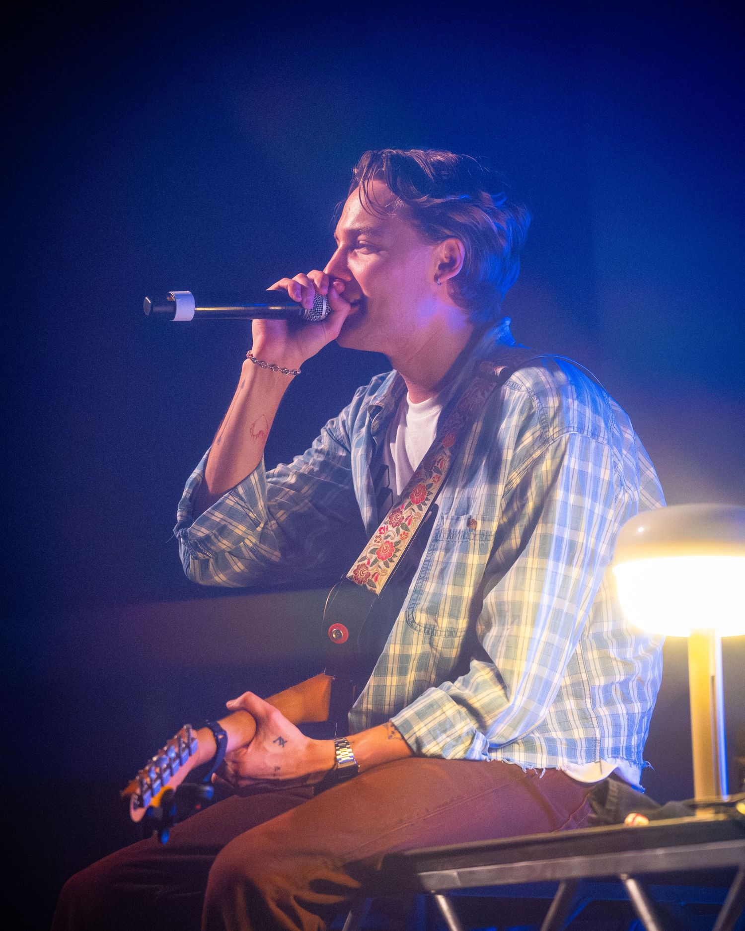 Concert performer singing into microphone while playing instrument on stage with blue lighting.