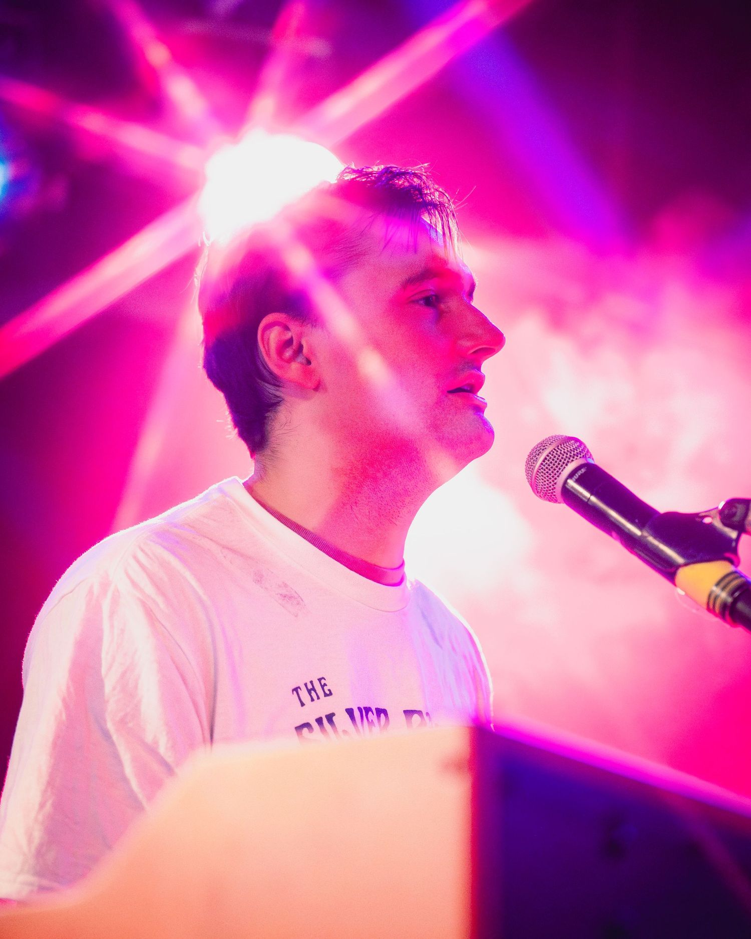 Concert performer singing under vibrant pink and purple stage lighting effects.