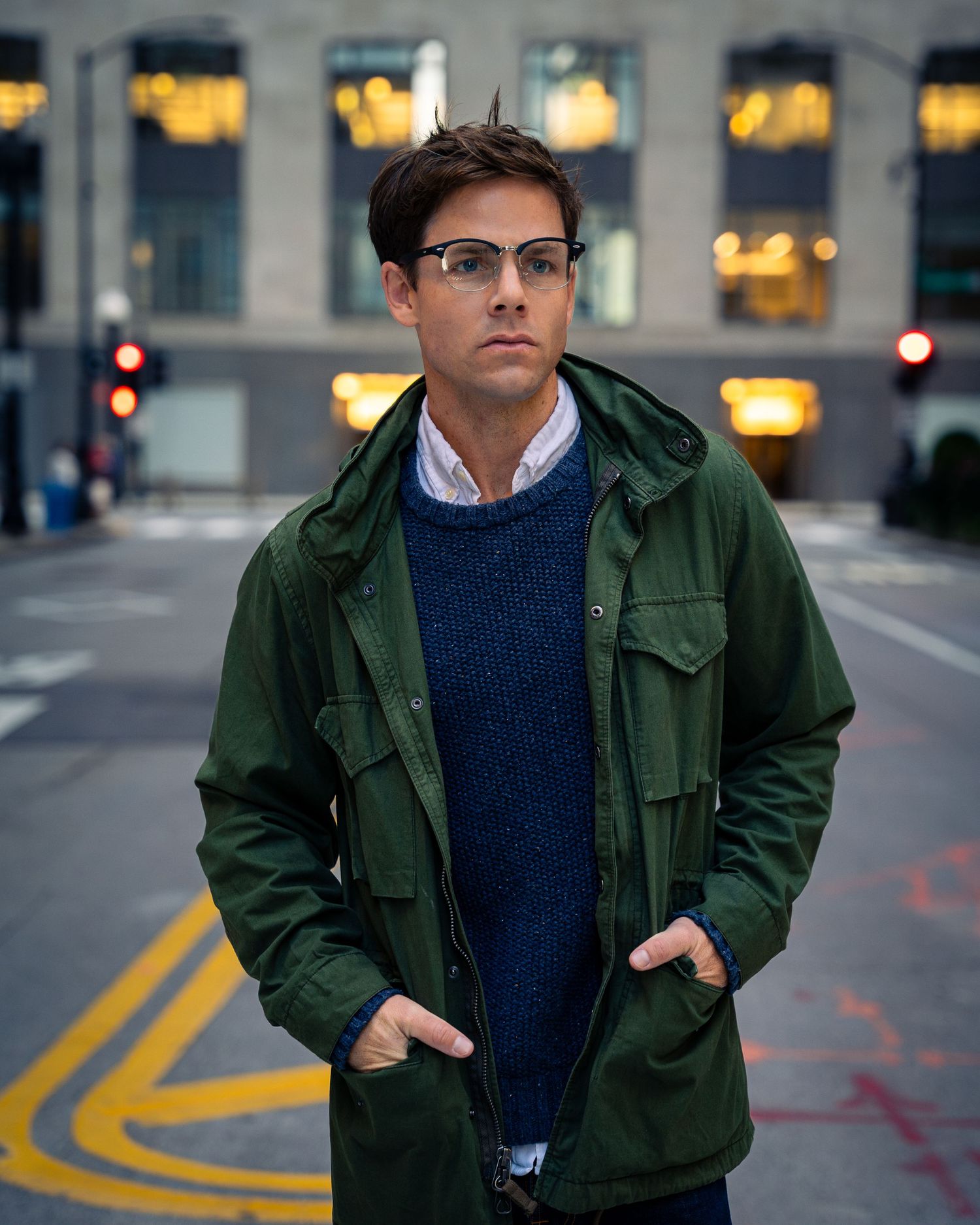 Person in green jacket and navy sweater walking in urban setting.