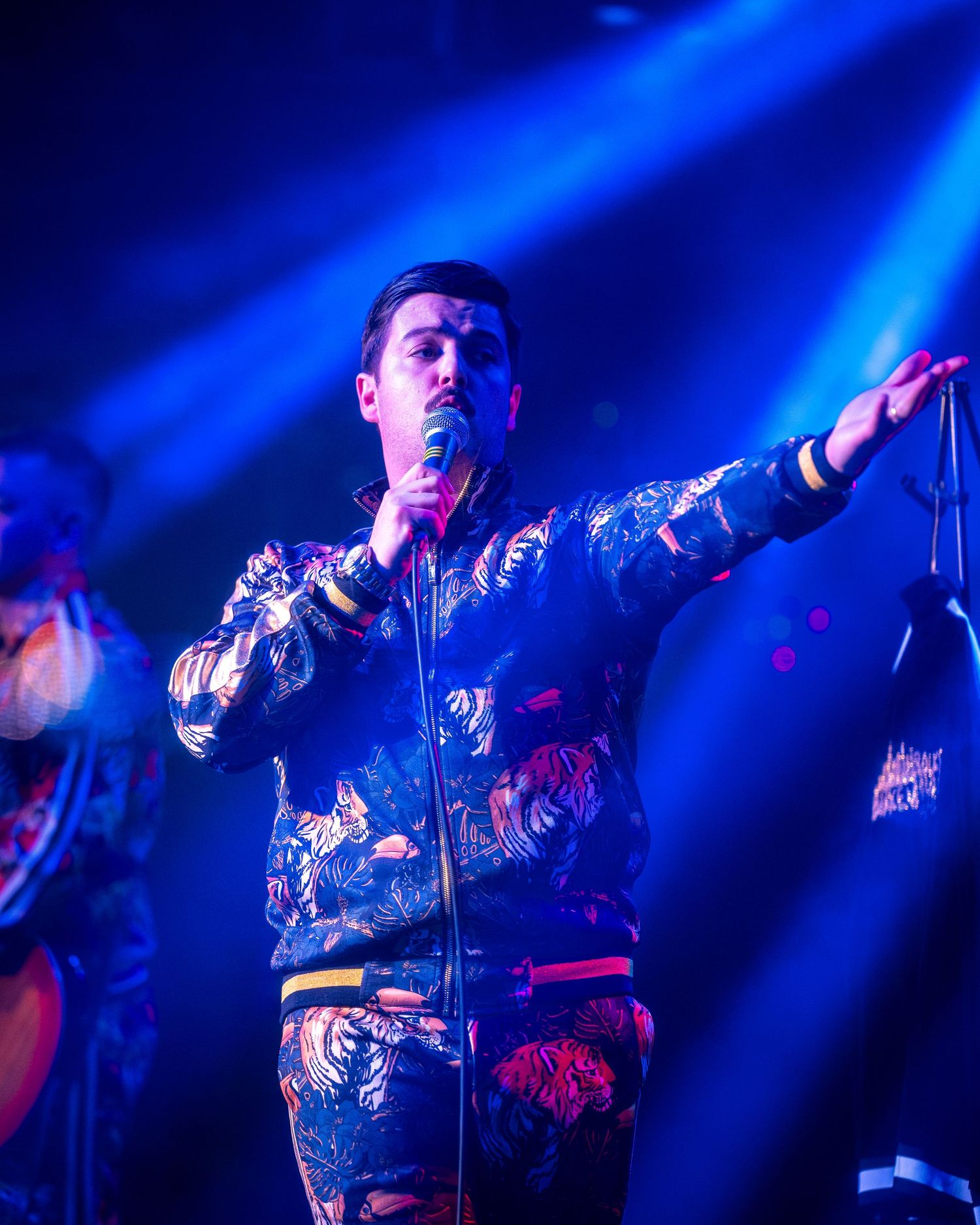 Performer in patterned jacket illuminated by dramatic blue stage lighting.