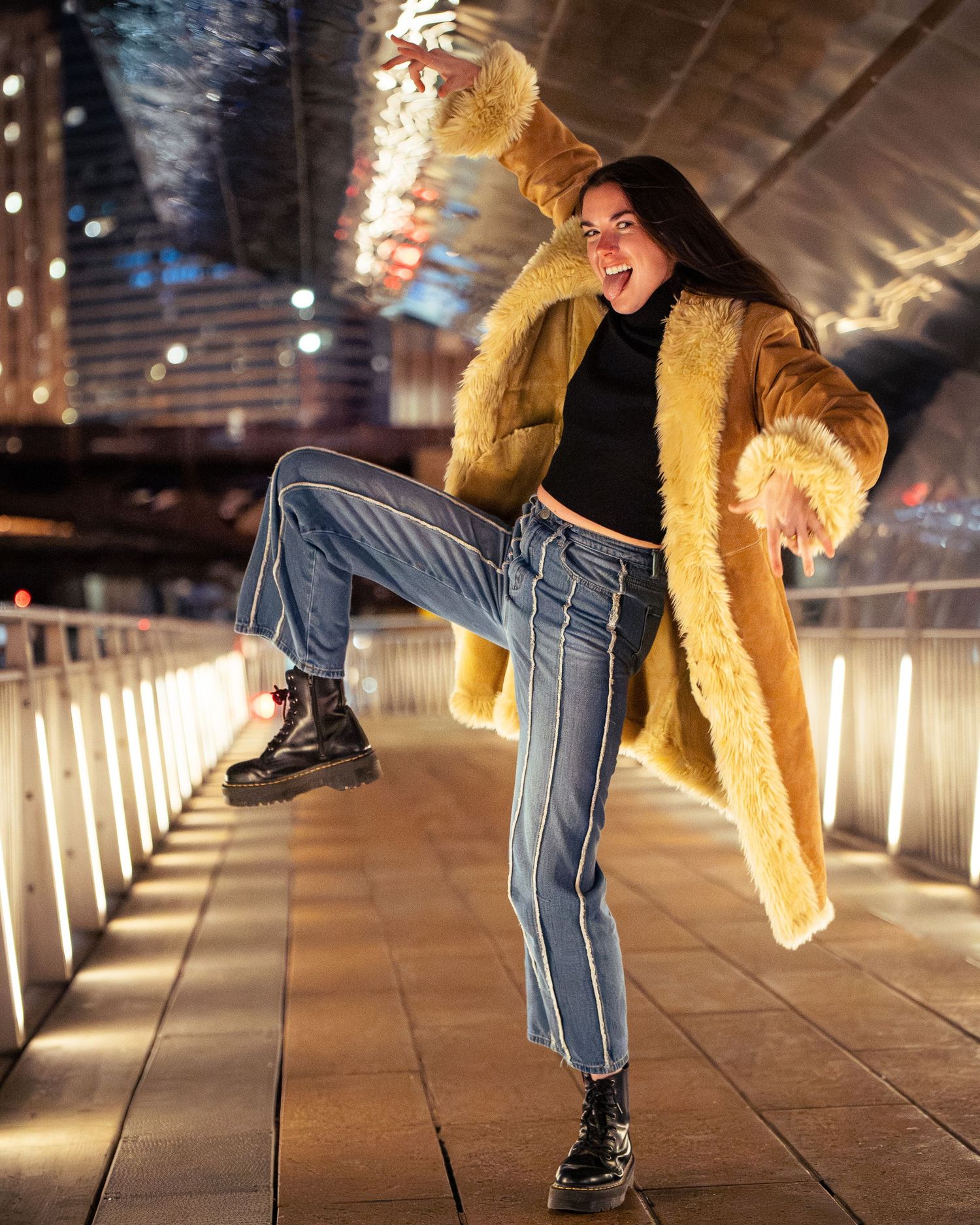 Person in tan furry coat and striped pants performs dance moves in an illuminated tunnel.