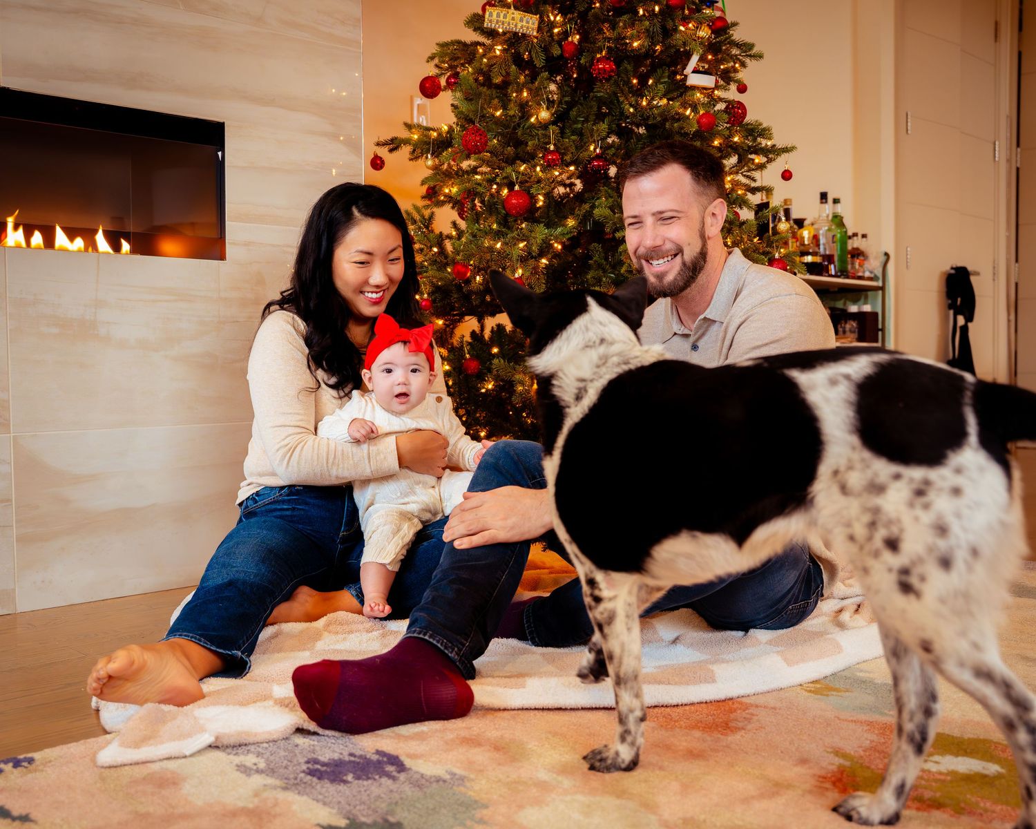 A group sits together on the floor writing holiday cards with a decorated Christmas tree visible in the background.
