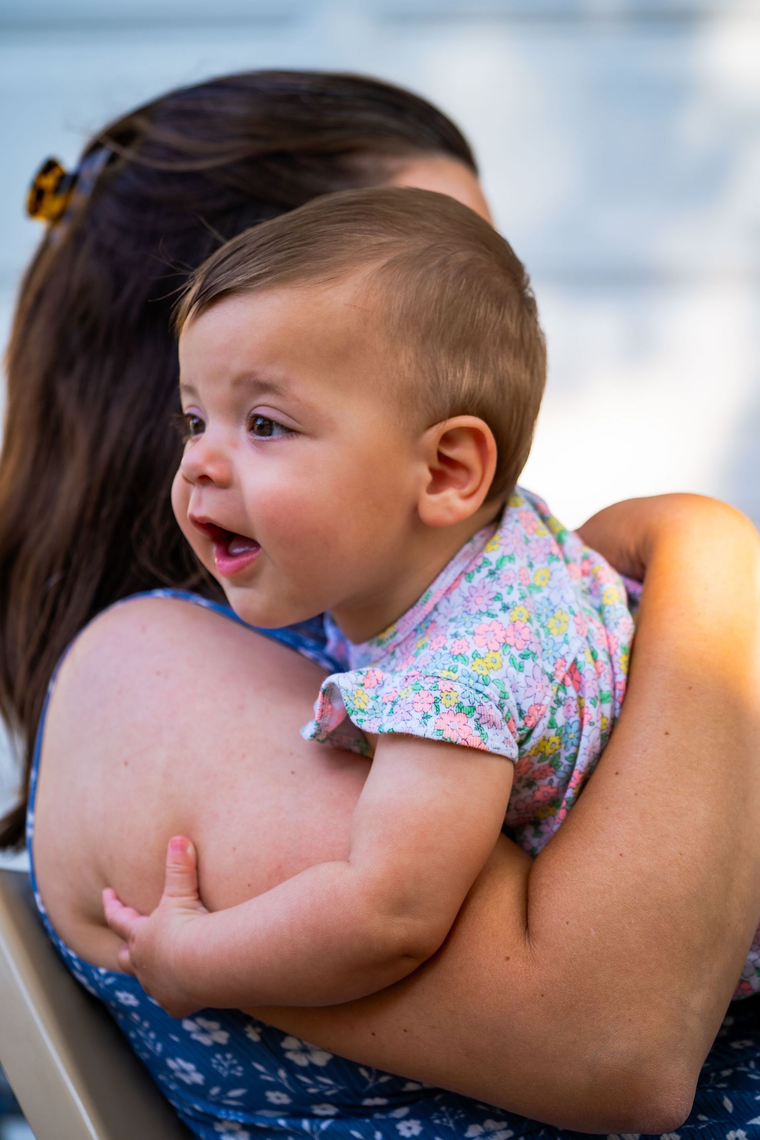 A small baby rests against someone's shoulder in a floral patterned outfit.